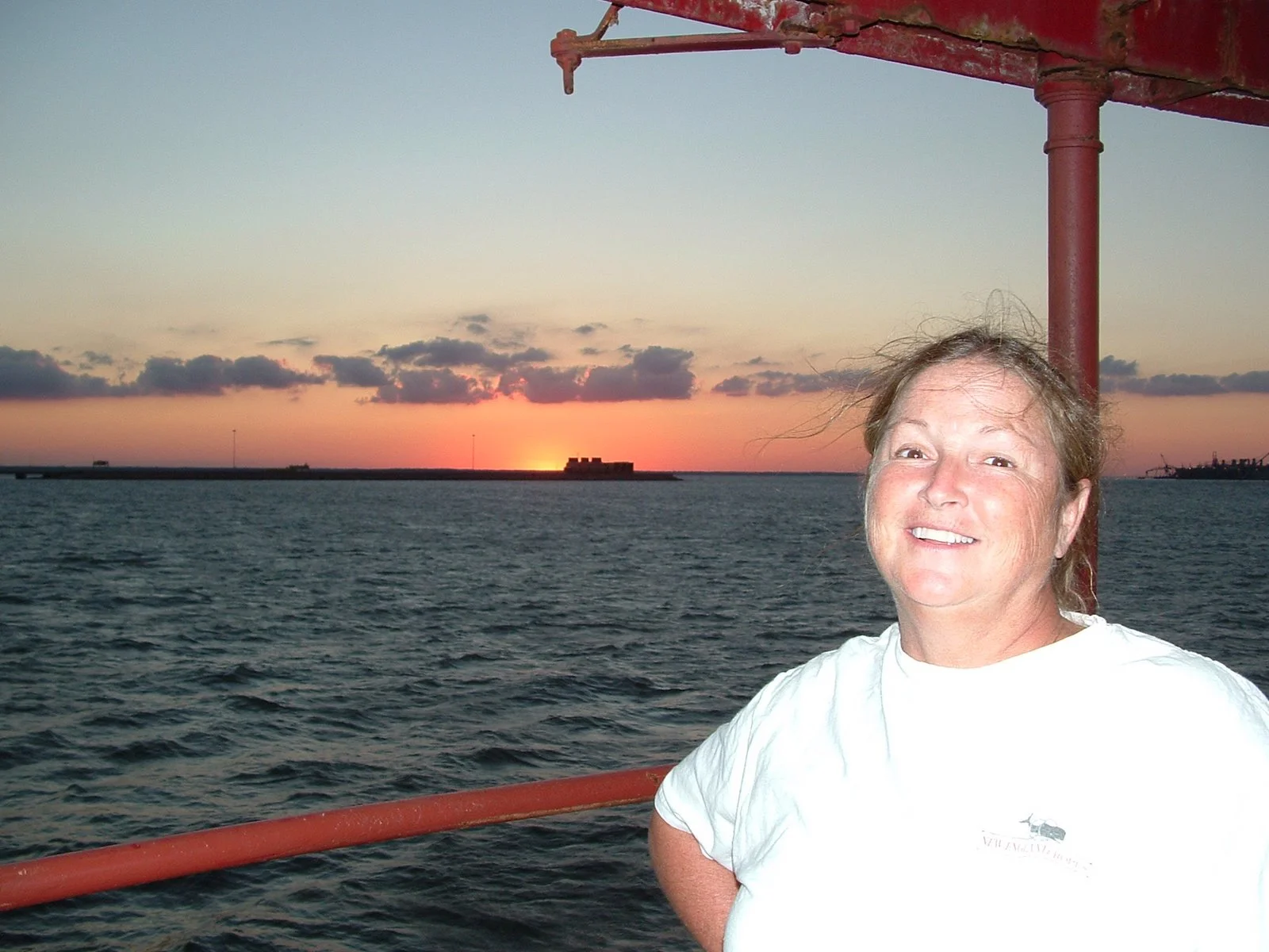 A woman smiling on Middle Ground Lighthouse at sunset, with water and Hampton Roads in the background.