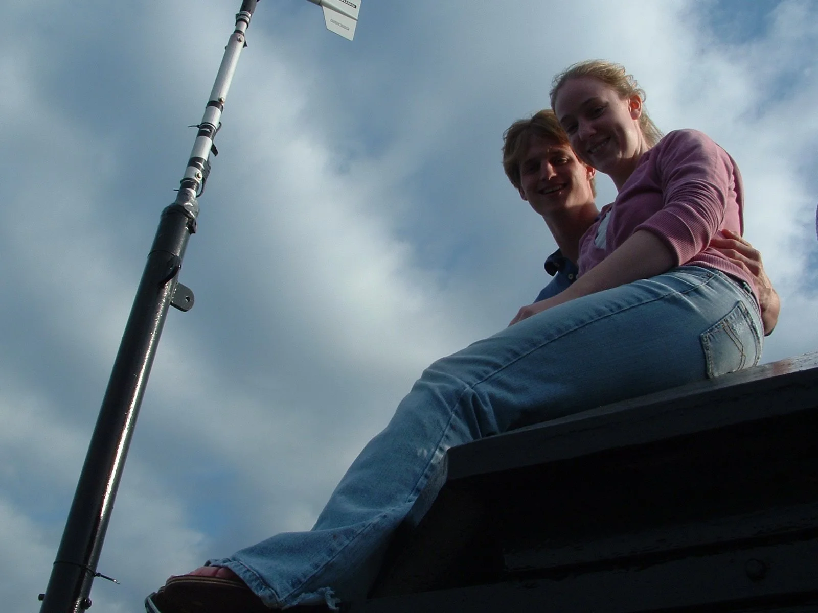 Two young people sitting close together on the lantern room roof of Middle Ground Lighthouse under a cloudy sky.