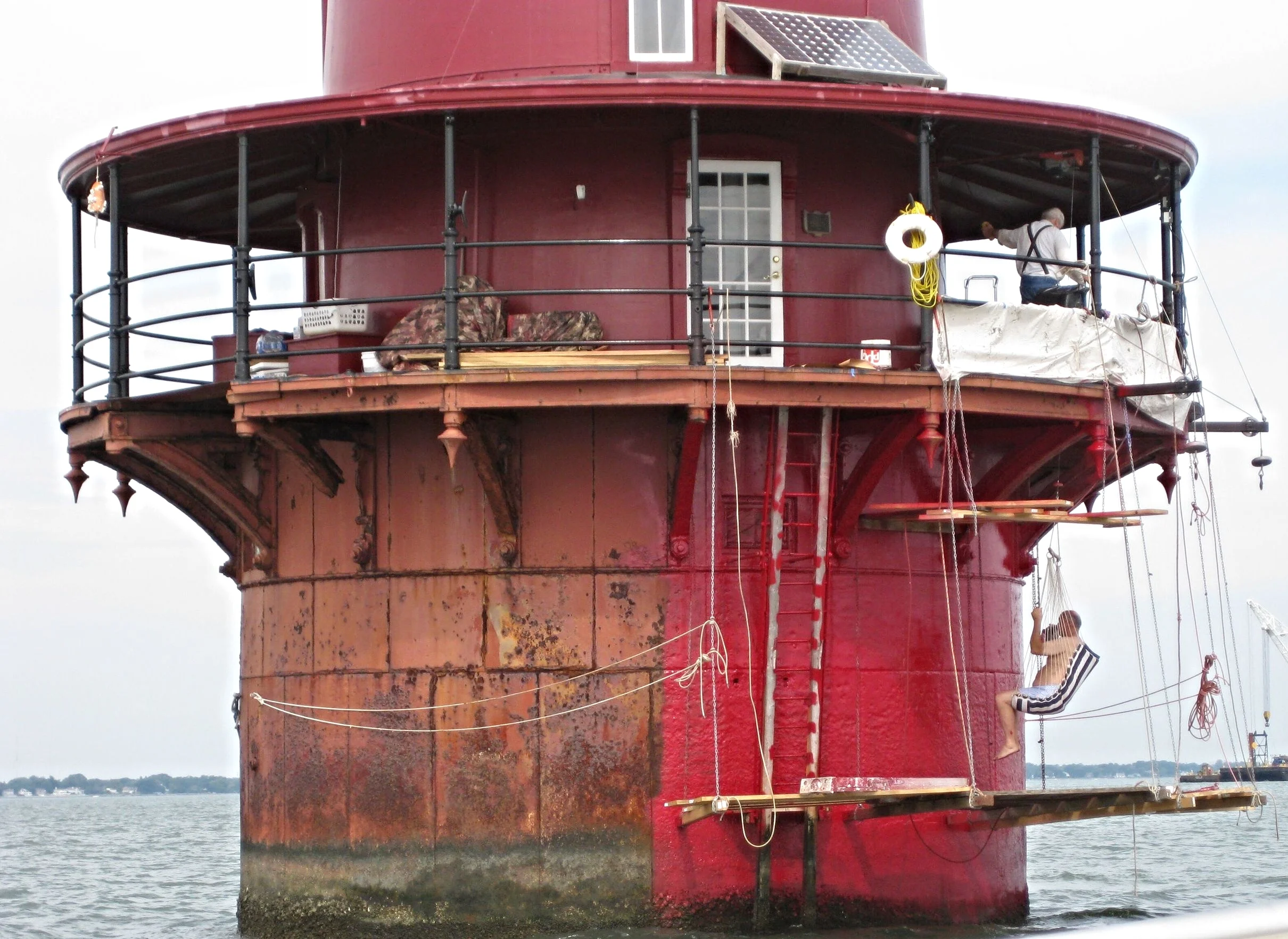 The exterior of Middle Ground Lighthouse getting a fresh coat of red paint from workers on scaffolding. 
