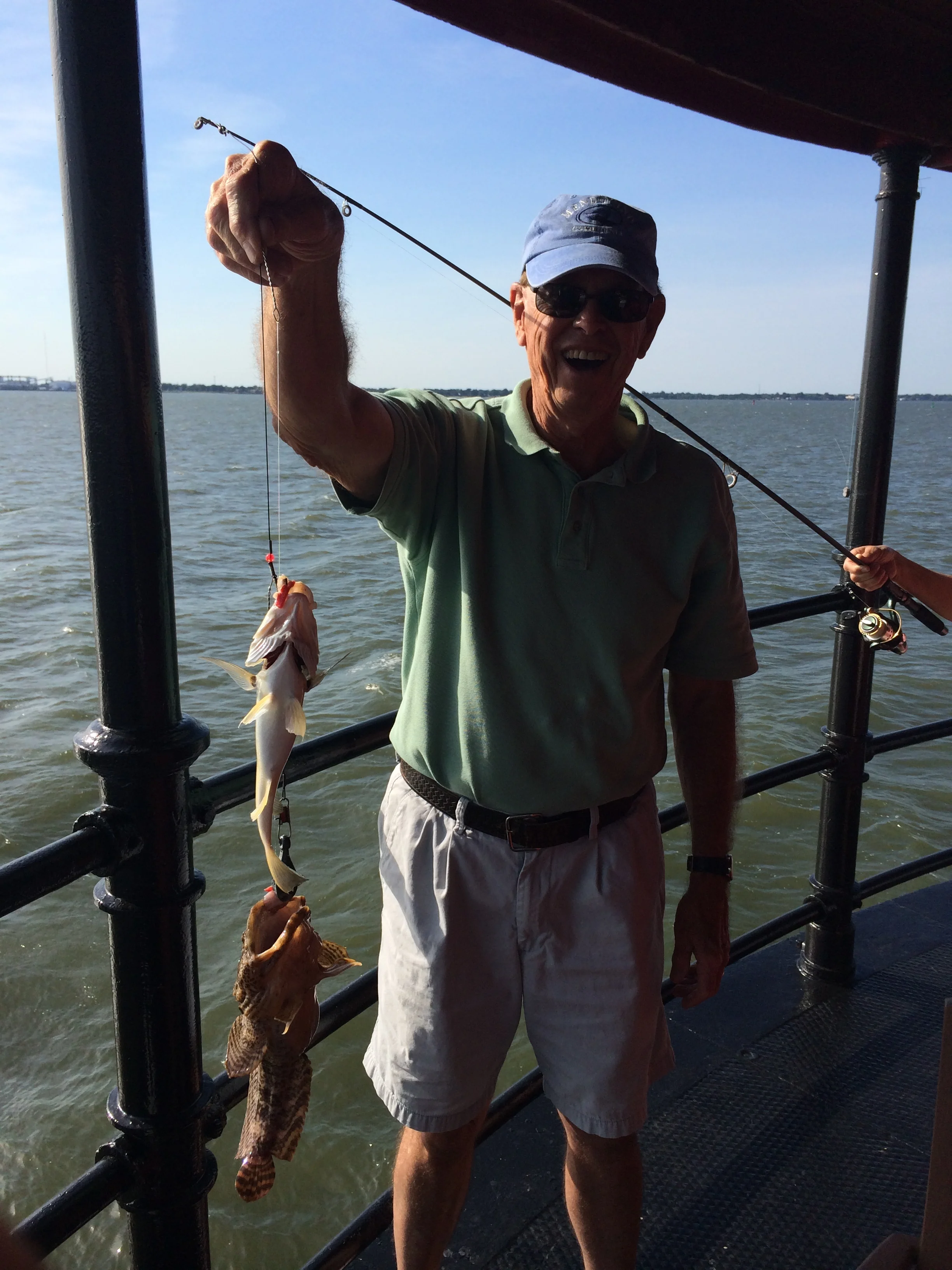 An elderly man on a boat holding up a line with a fish caught on a fishing hook on Middle Ground Lighthouse.