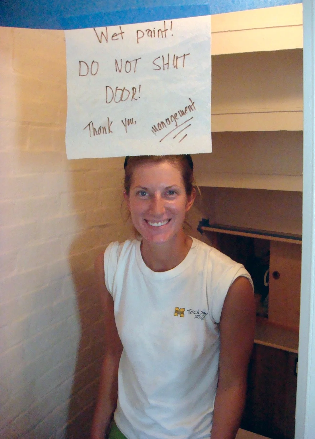 A worker painting the bathroom on the kitchen level of Middle Ground Lighthouse with a sign that reads "Wet paint! Do not shut door! Thank you, management".