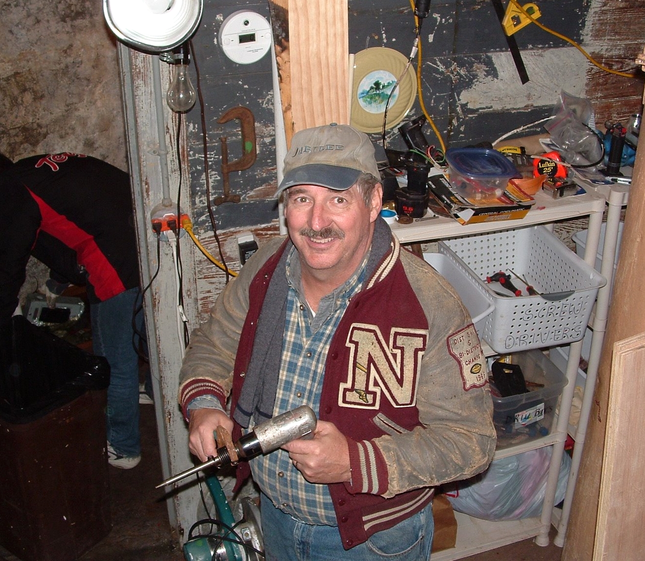 A smiling man holding a soldering iron in the cellar workshop of Middle Ground Lighthouse. 
