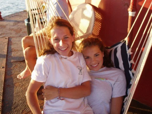 Two young girls smiling and relaxing in hanging chairs on Middle Ground Lighthouse near the water at sunset.