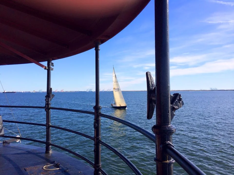 View from Middle Ground Lighthouse showing a sailboat in the water under a blue sky.