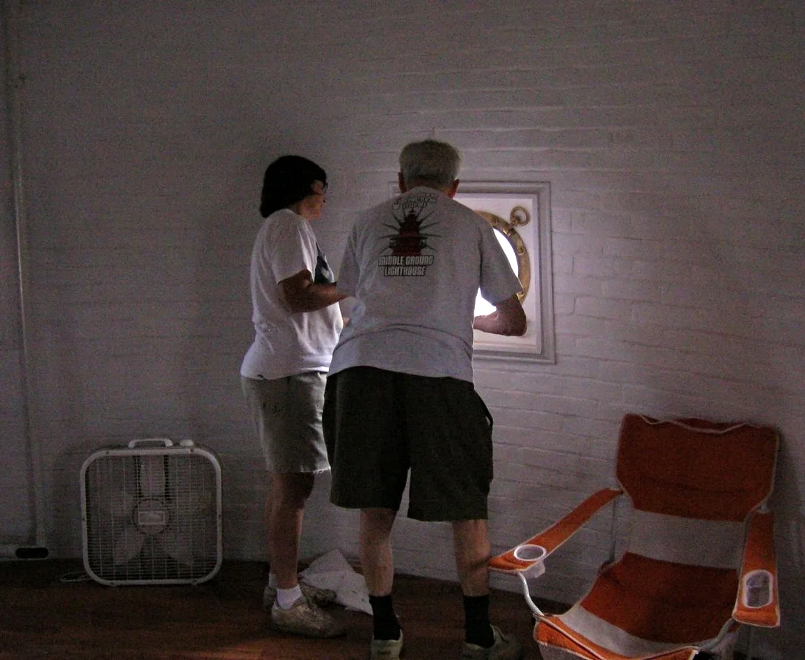 Two people measuring for and installing new porthole windows in the porthole room of Middle Ground Lighthouse. 