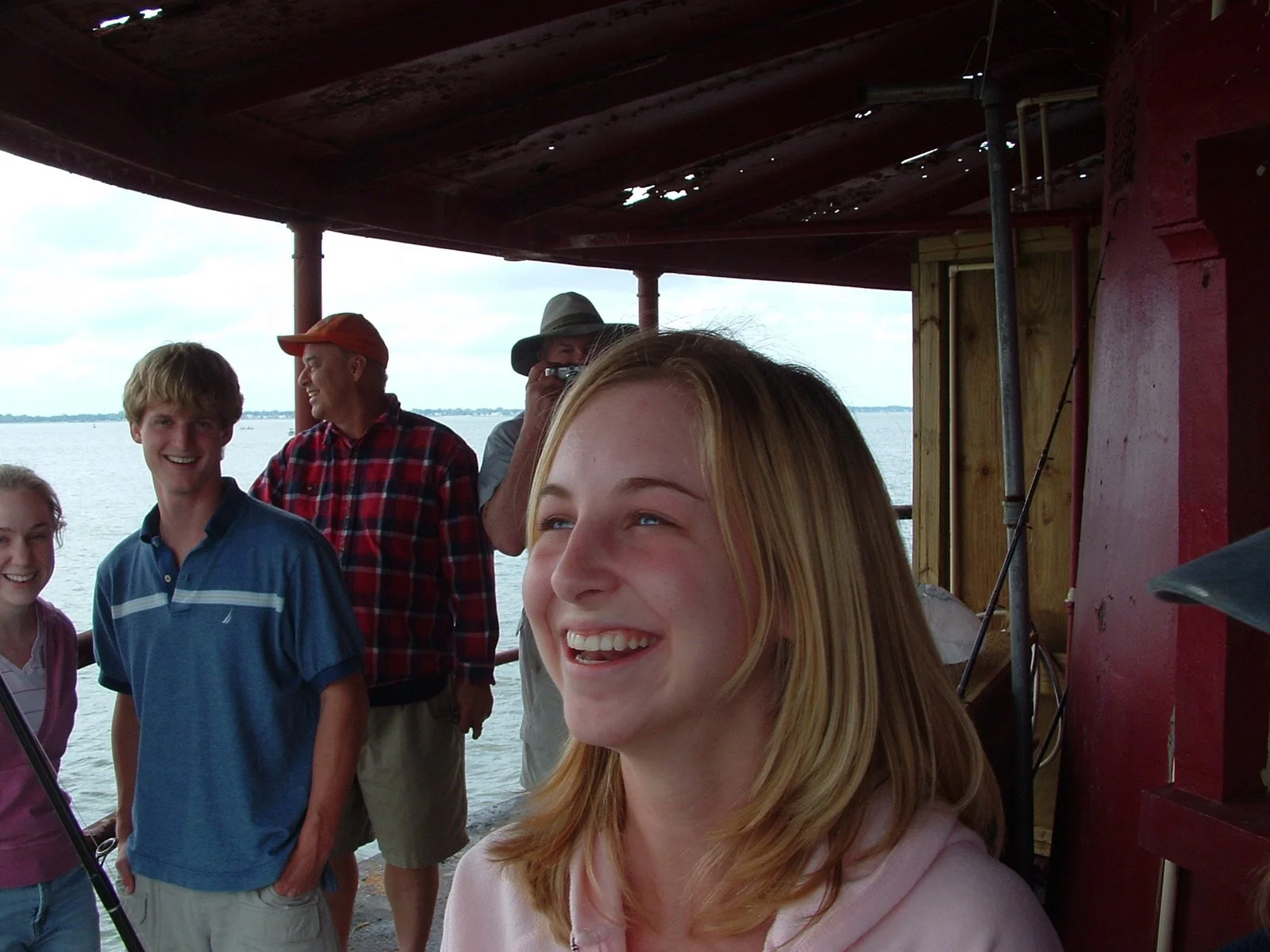 A group of smiling people on Middle Ground Lighthouse with water and sky in the background, including a young woman with blonde hair in the foreground who caught a fish.