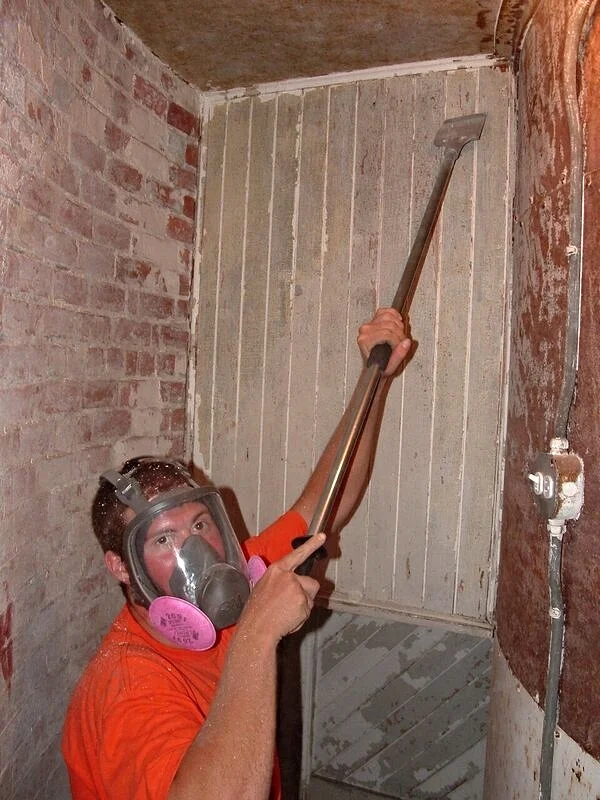 A worker wearing a mask scraping paint inside the construction of Middle Ground Lighthouse during restoration. 