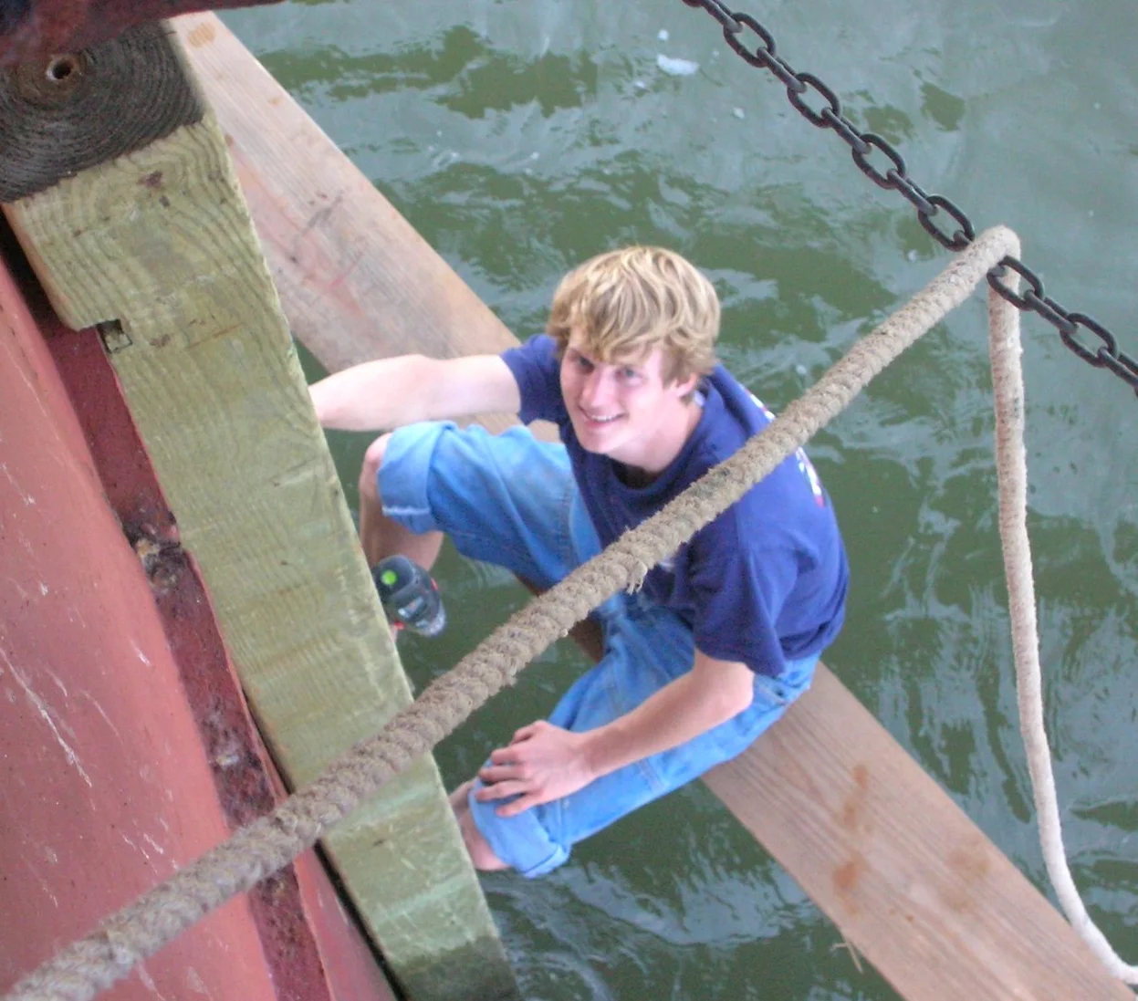 A young worker on scaffolding painting the exterior of Middle Ground Lighthouse near the waterline. 