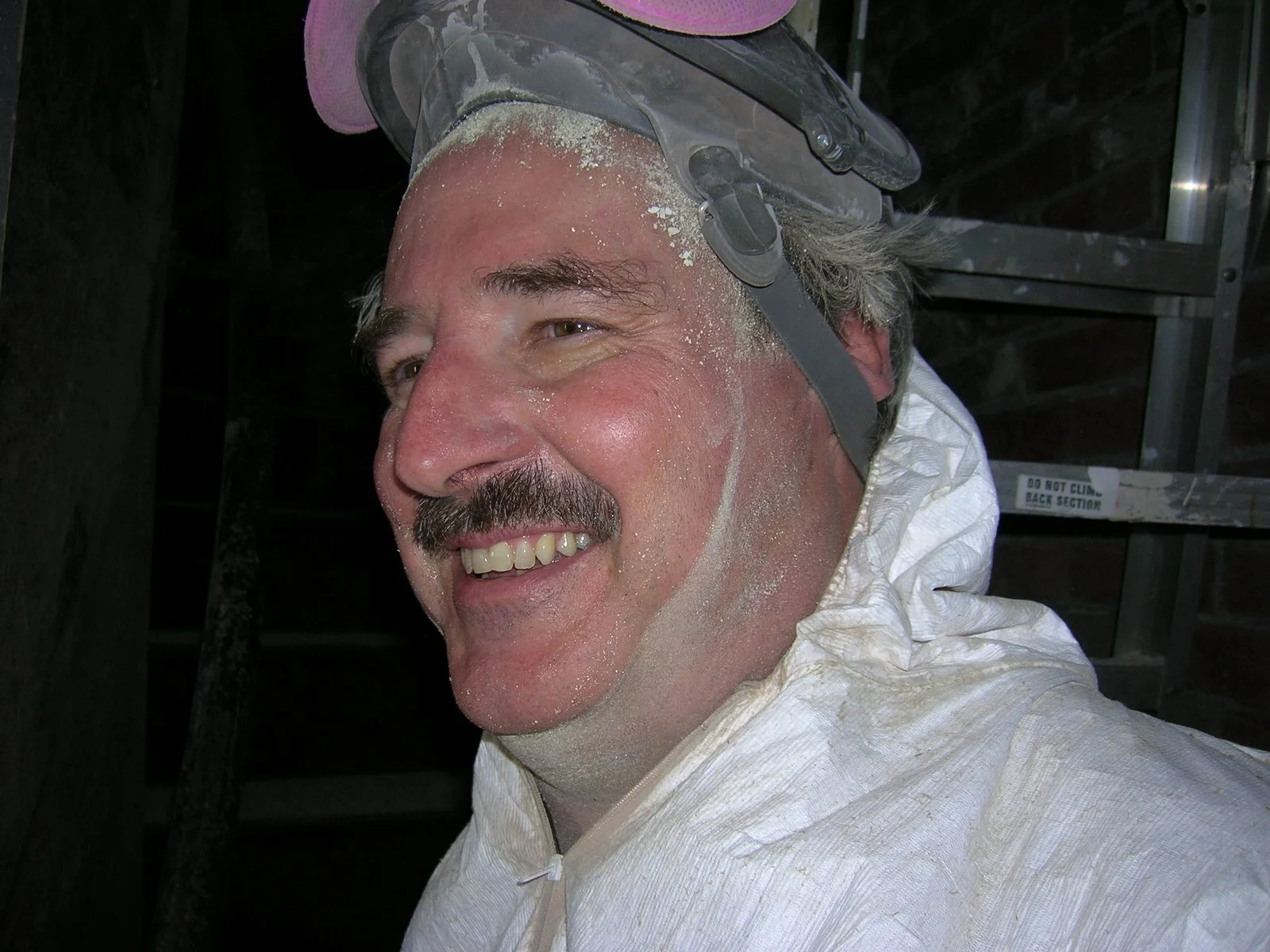A man wearing a safety helmet and a white protective suit suit, with dust or dirt on his face and suit on Middle Ground Lighthouse. 