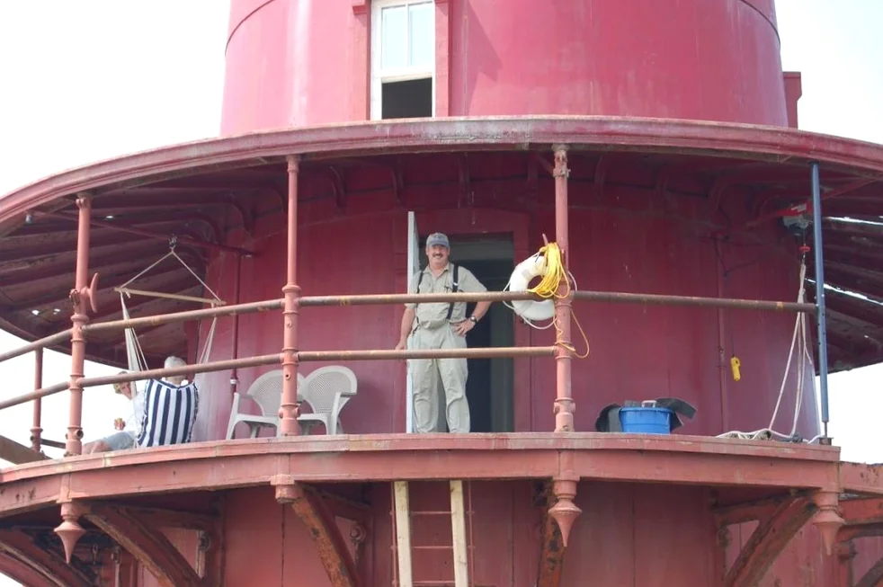 Person standing on the balcony of Middle Ground Lighthouse with a person sitting in a hammock on the left side of the balcony.
