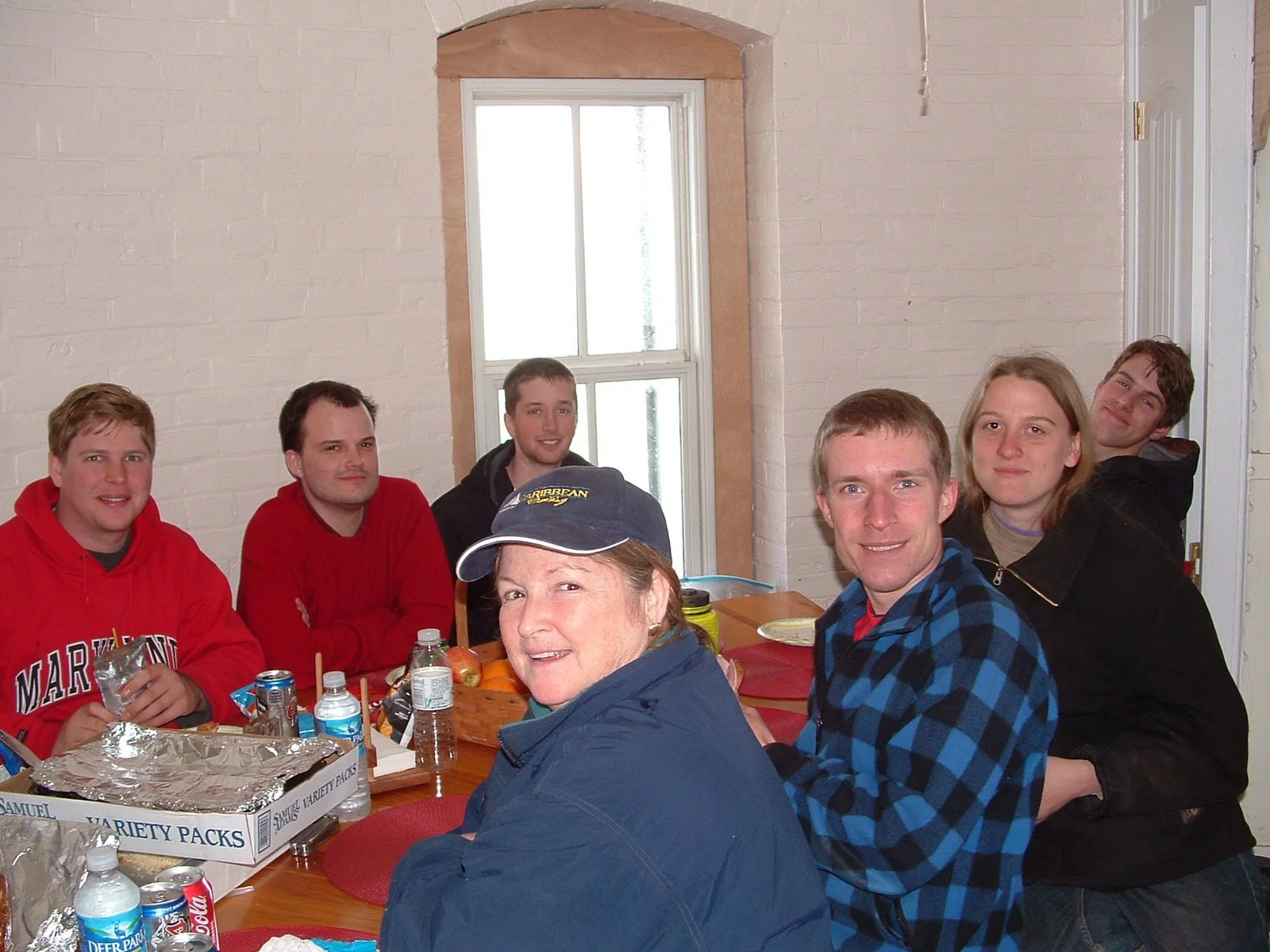Group of seven people sitting around a table in the kitchen of Middle Ground Lighthouse, having a meal or gathering.