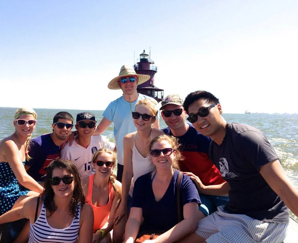 Group of friends on a boat near Middle Ground Lighthouse on the water during sunny weather, all wearing sunglasses.