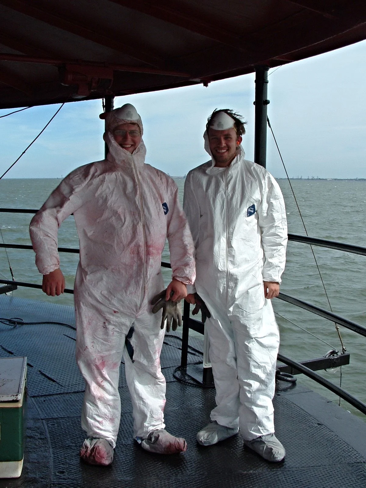 Two people dressed in white protective suits standing on Middle Ground Lighthouse, removing lead paint. 
