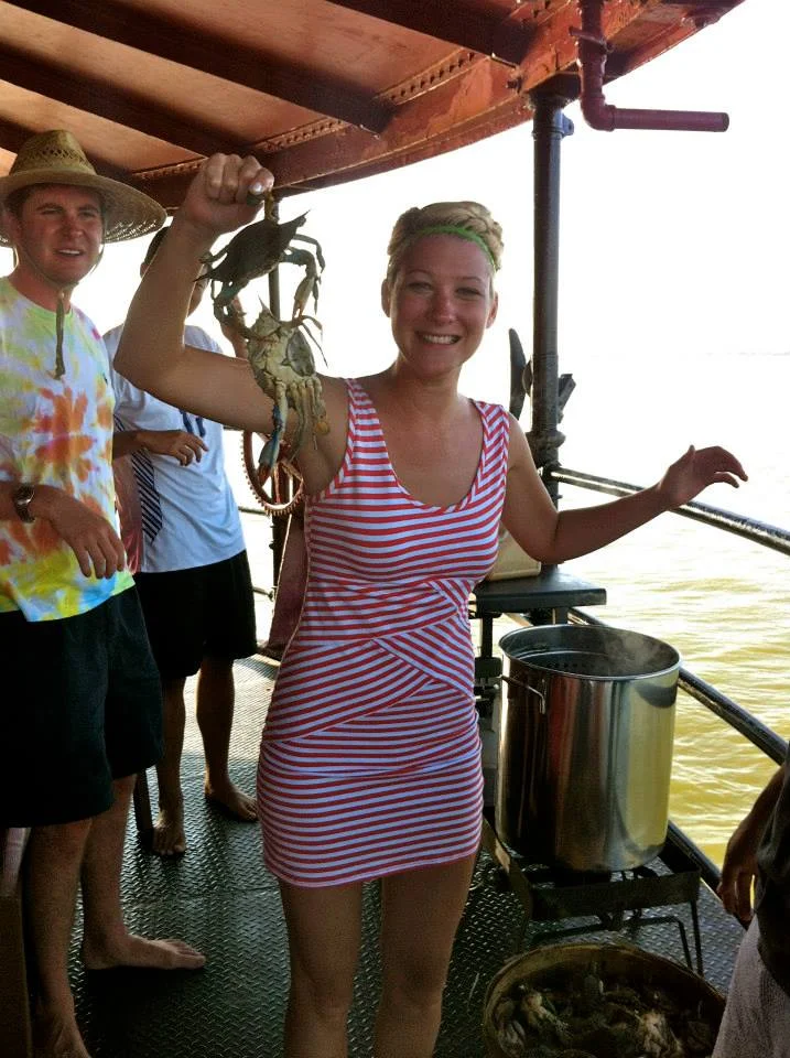Woman in a red and white striped dress holding a caught crab on Middle Ground Lighthouse with other people.