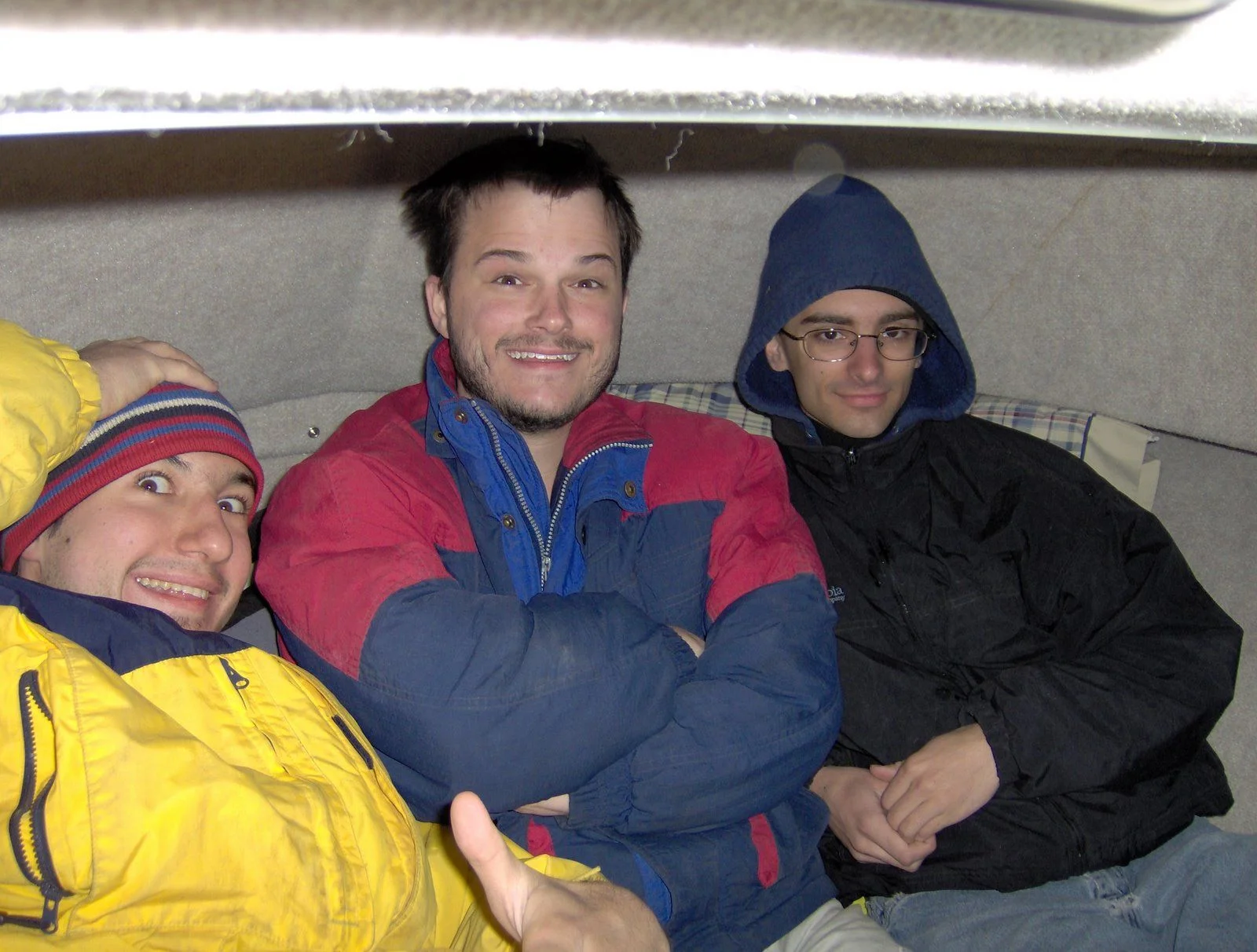 Three men sitting close together, smiling, dressed in warm clothing and jackets, inside a small boat.