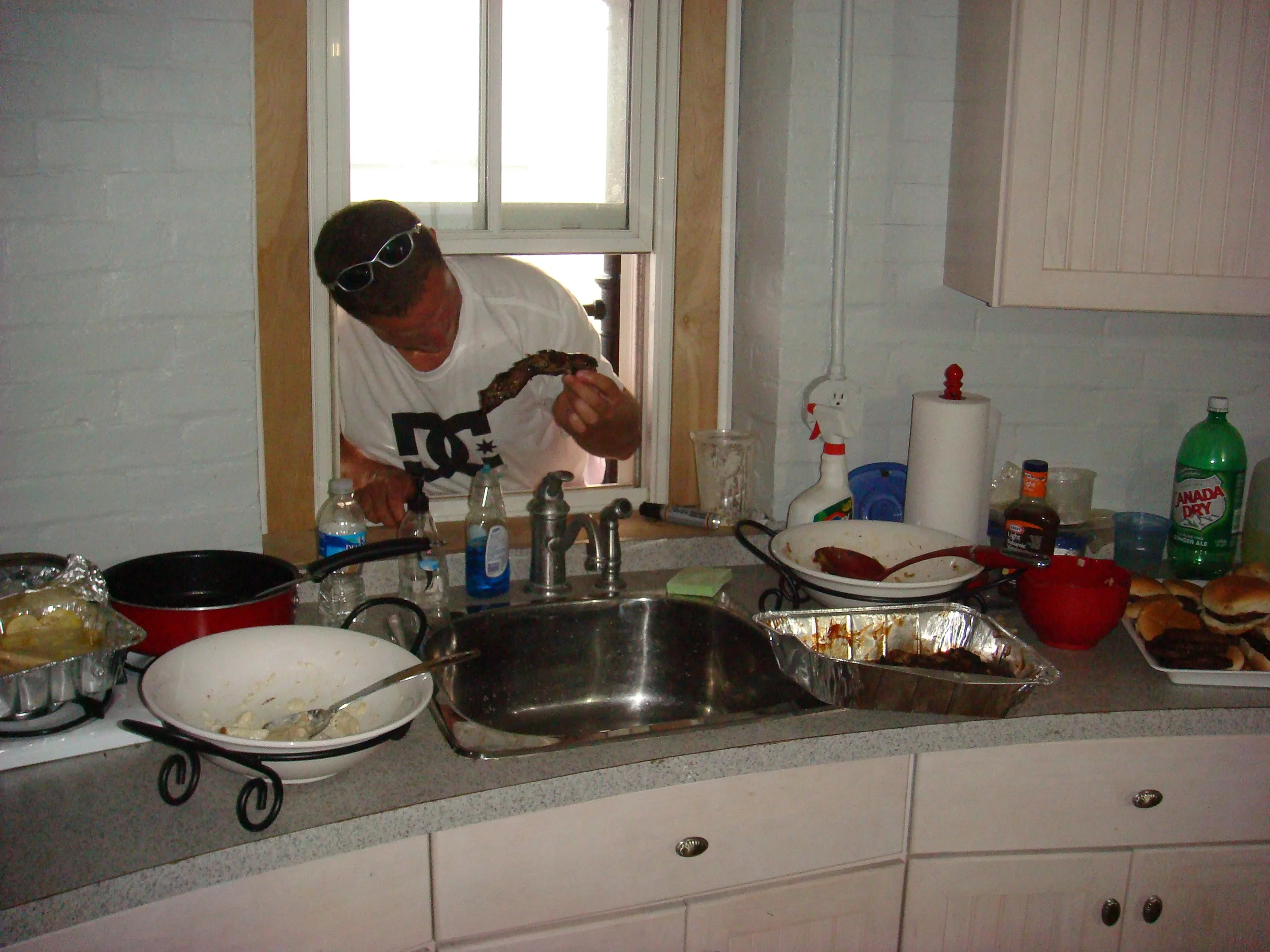 A man looks through the kitchen window of Middle Ground Lighthouse while holding a piece of meat that was cooked on the grill outside. 