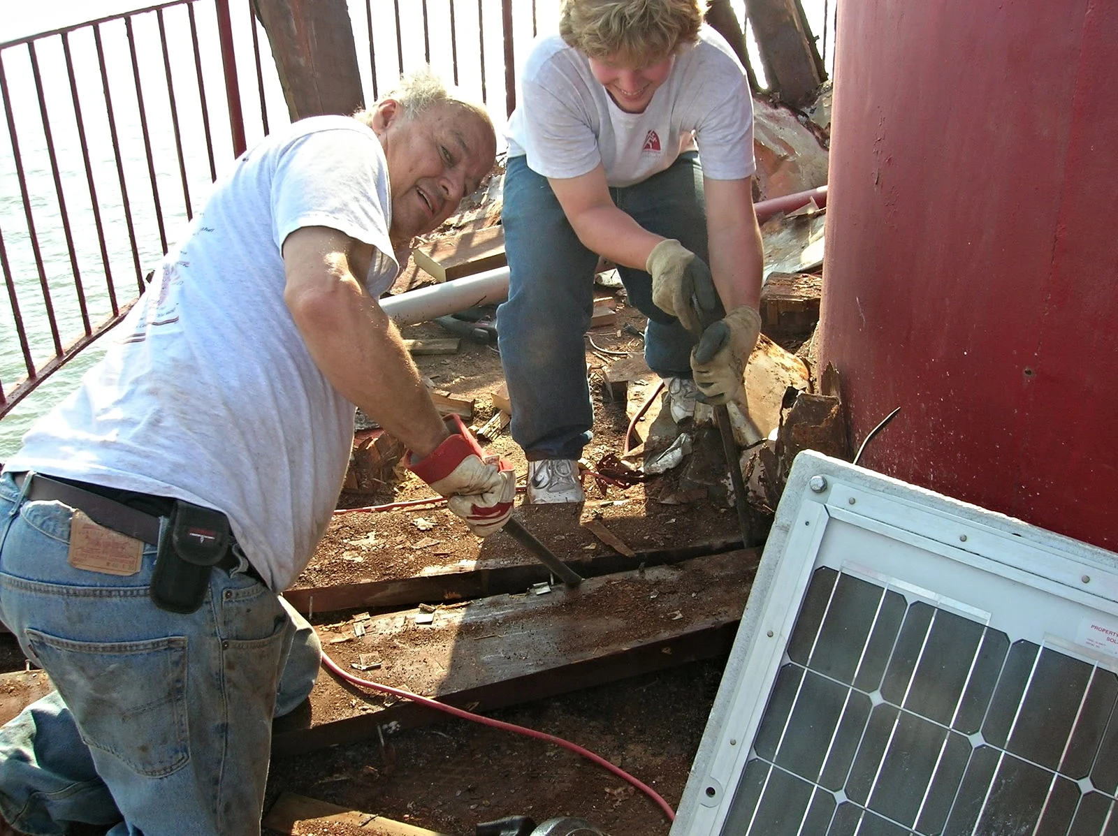 Two workers removing the damaged decking of the watch room balcony of Middle Ground Lighthouse. 