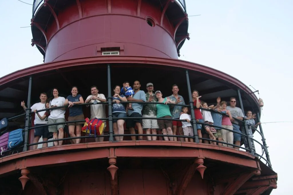 Group of people standing on the balcony of Middle Ground Lighthouse, smiling and waving.