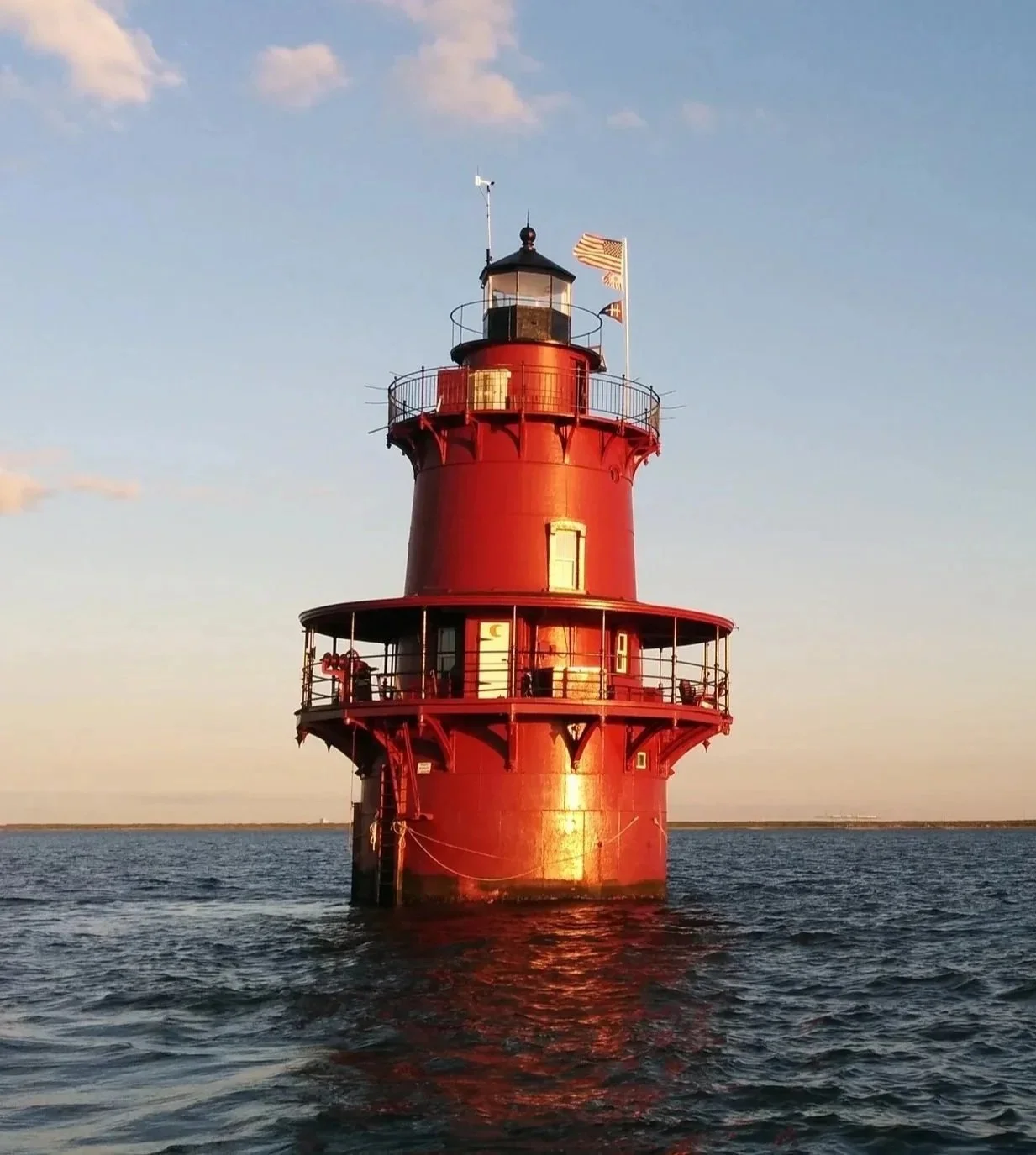 Middle Ground Lighthouse on the water, with a clear sky and a few clouds, during sunset.