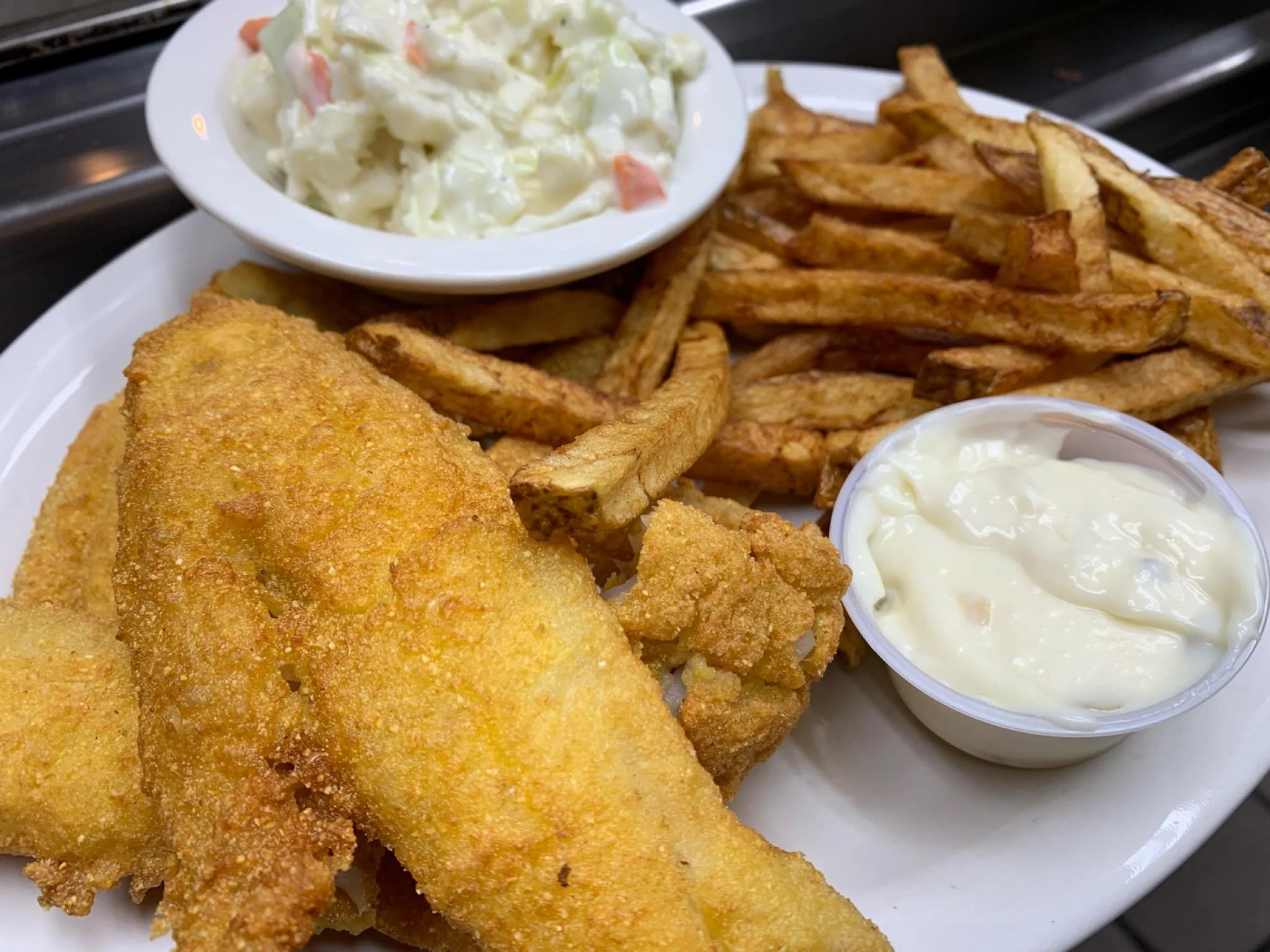 Plate of fried fish, French fries, coleslaw, and a cup of tartar sauce.