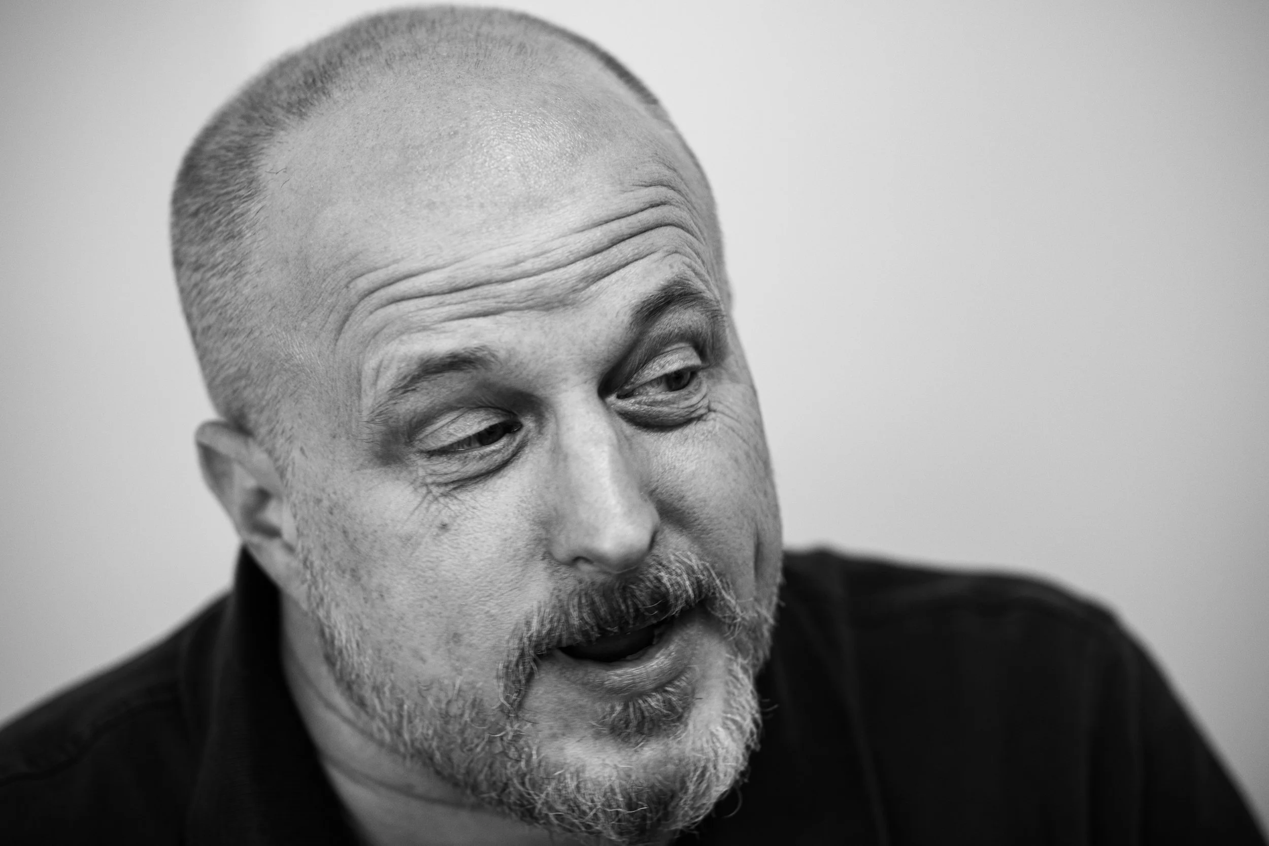 Black and white close-up of Tim Cifelli, with a bearded face, short hair, and expressive facial features, looking to the side.