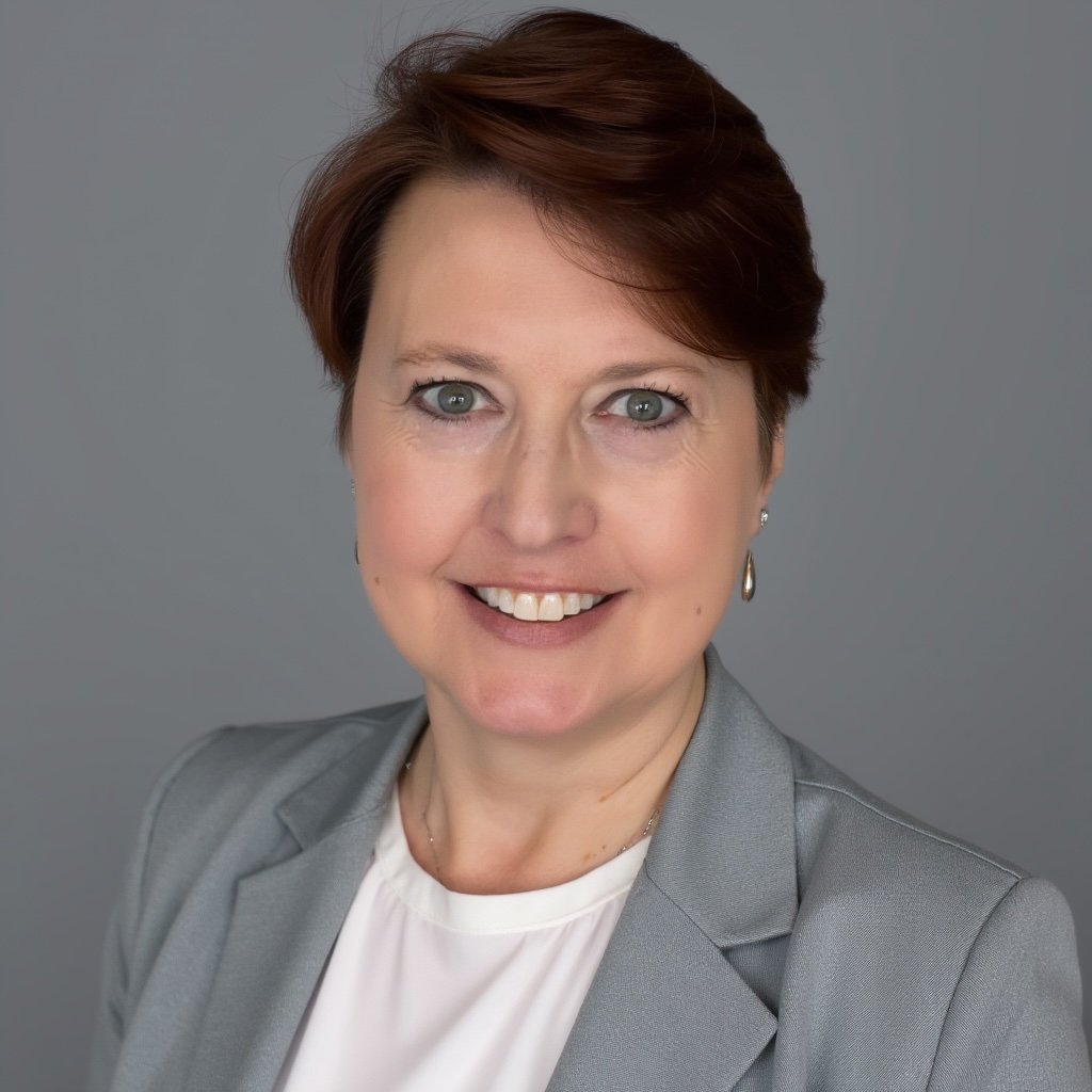 A professional woman with short reddish-brown hair smiling, wearing a gray blazer and earrings, posed against a gray background.