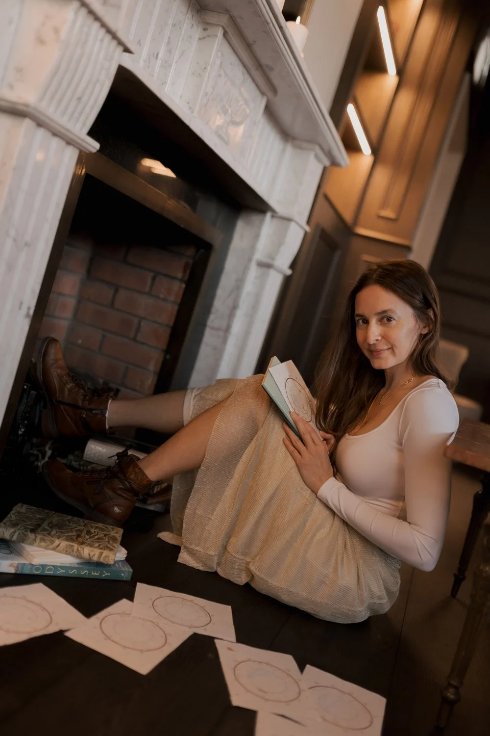 Rachelle Hicks, online astrologer, reading a mythology book in a warm, intimate setting