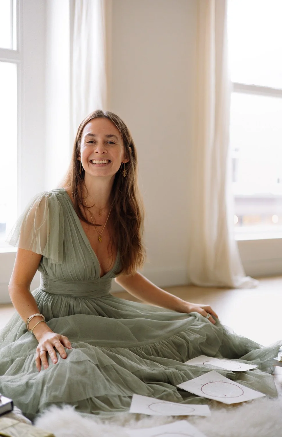 Rachelle Hicks, online astrologer, sitting with birth chart drawings and smiling in a light-filled space