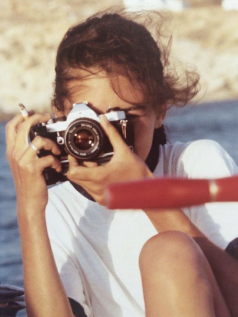 Person with short hair taking a photograph with a vintage film camera outdoors.