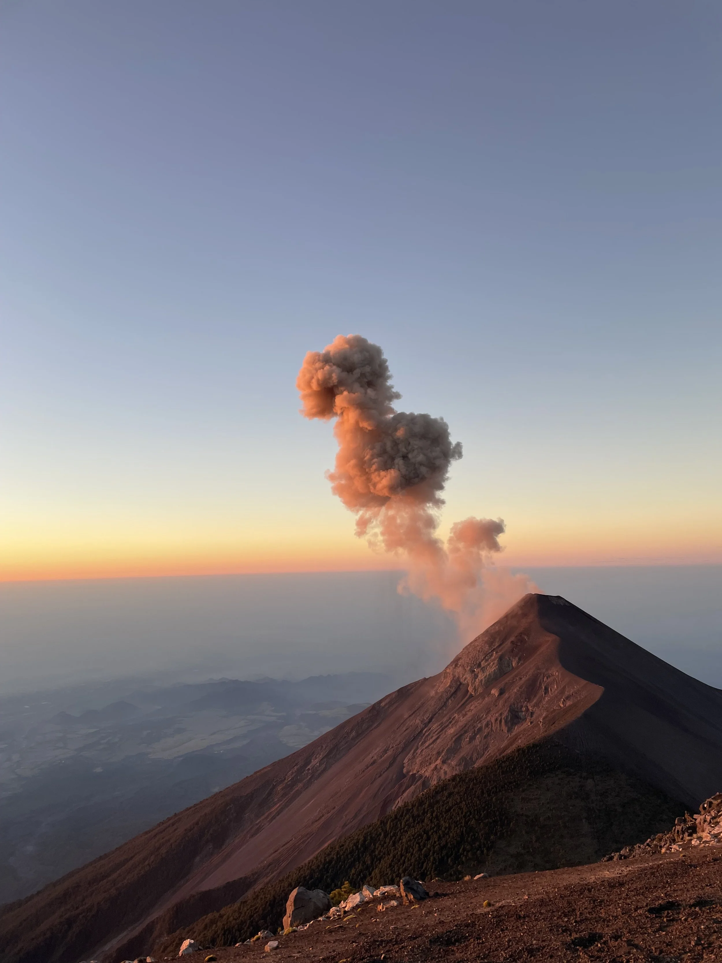 Active volcano emitting ash and smoke during sunset.