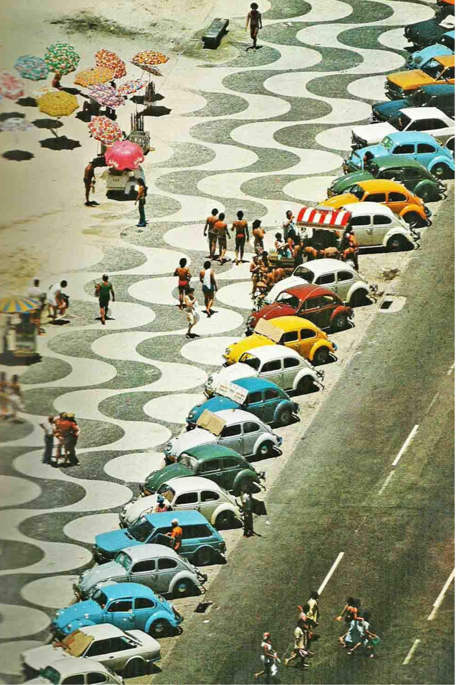 Colorful vintage cars parked along a street with people walking and shopping, and umbrellas providing shade on a patterned sidewalk.
