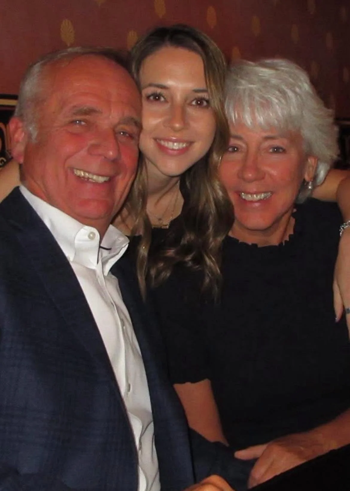 Three people smiling and posing together indoors, likely at a social event or gathering.