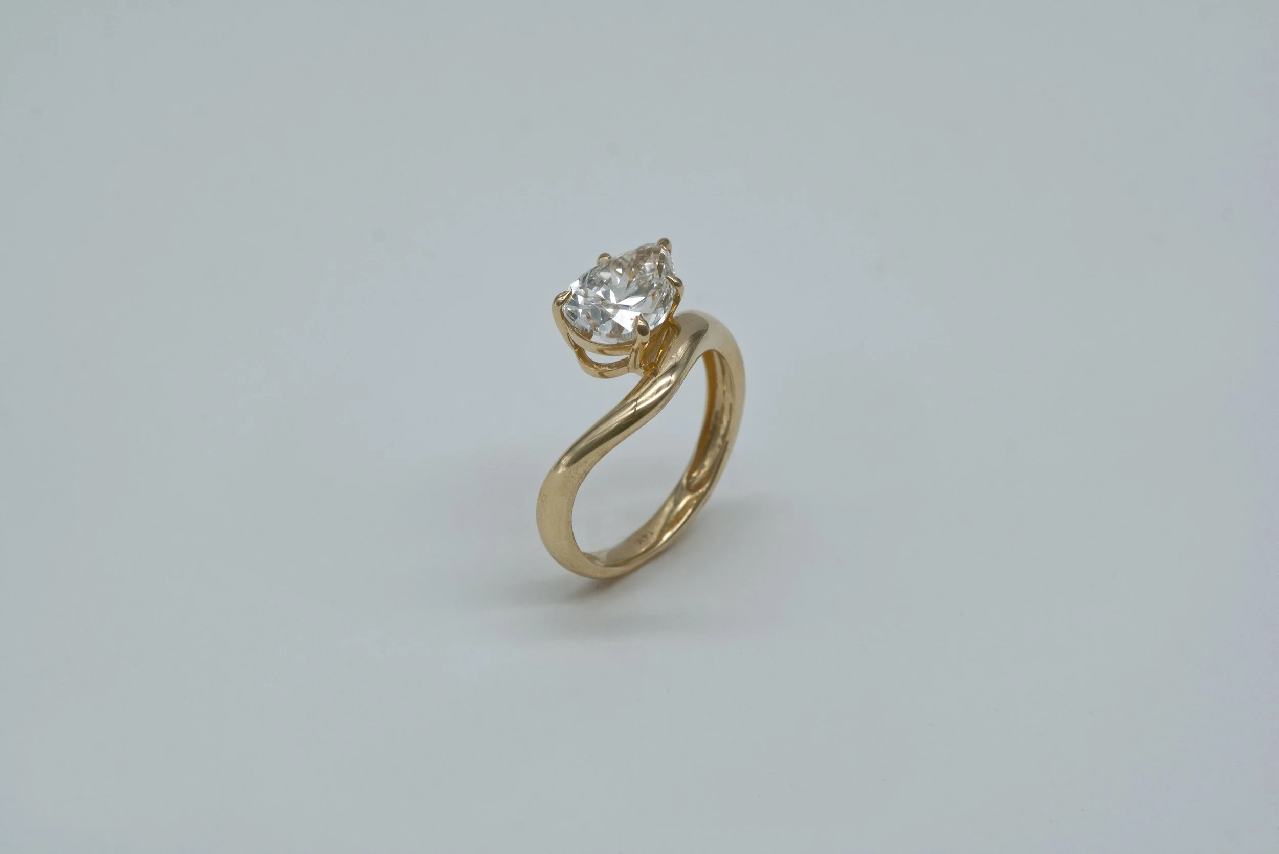 A gold ring with a large, clear, pear-shaped diamond solitaire setting on a plain, light background.