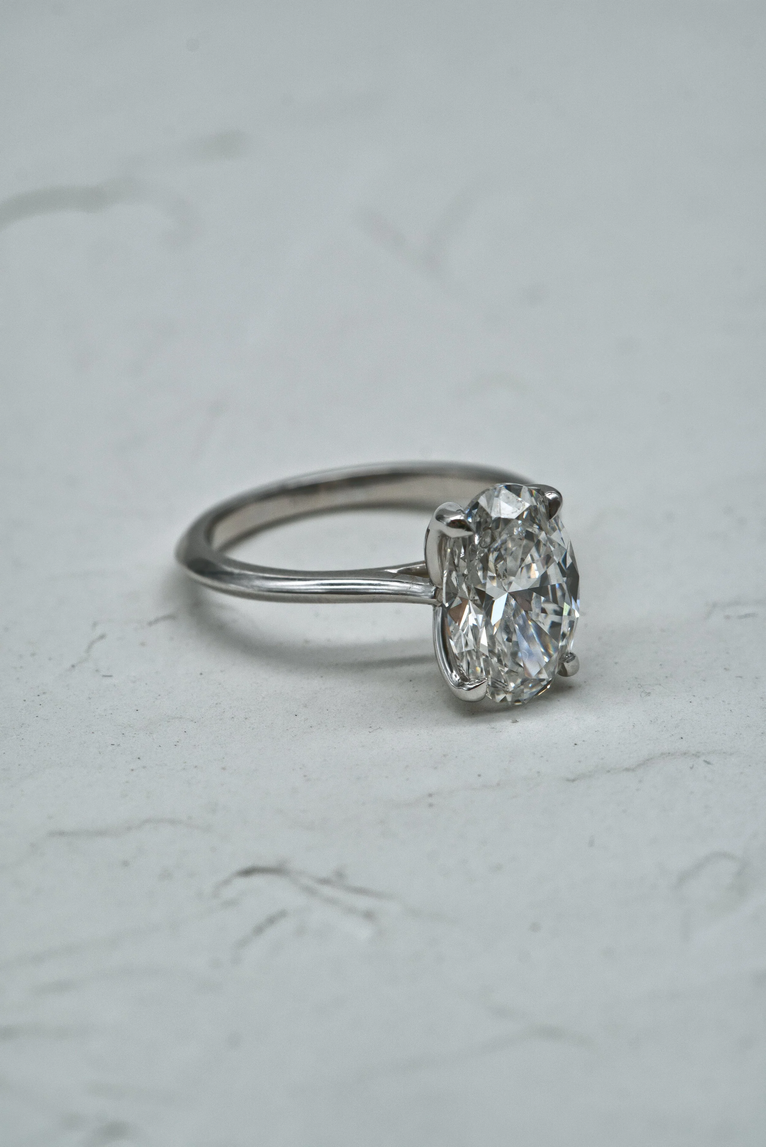 A close-up view of a silver engagement ring with a large oval-cut diamond, set on a plain white surface.