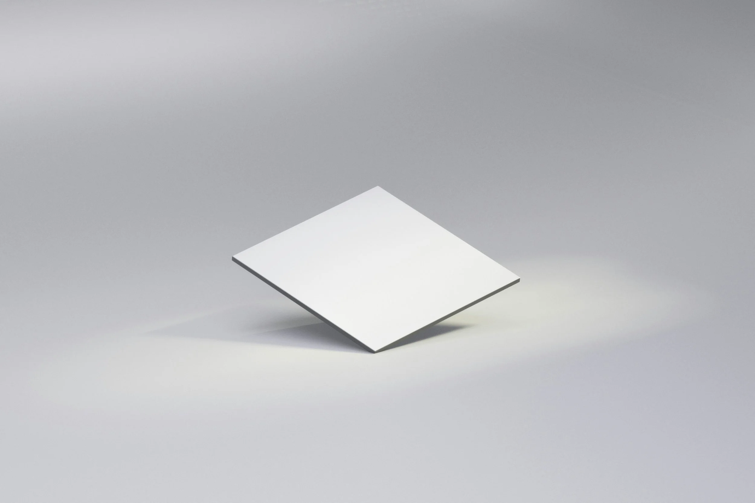 A white square tile tilted and floating above a light gray surface.