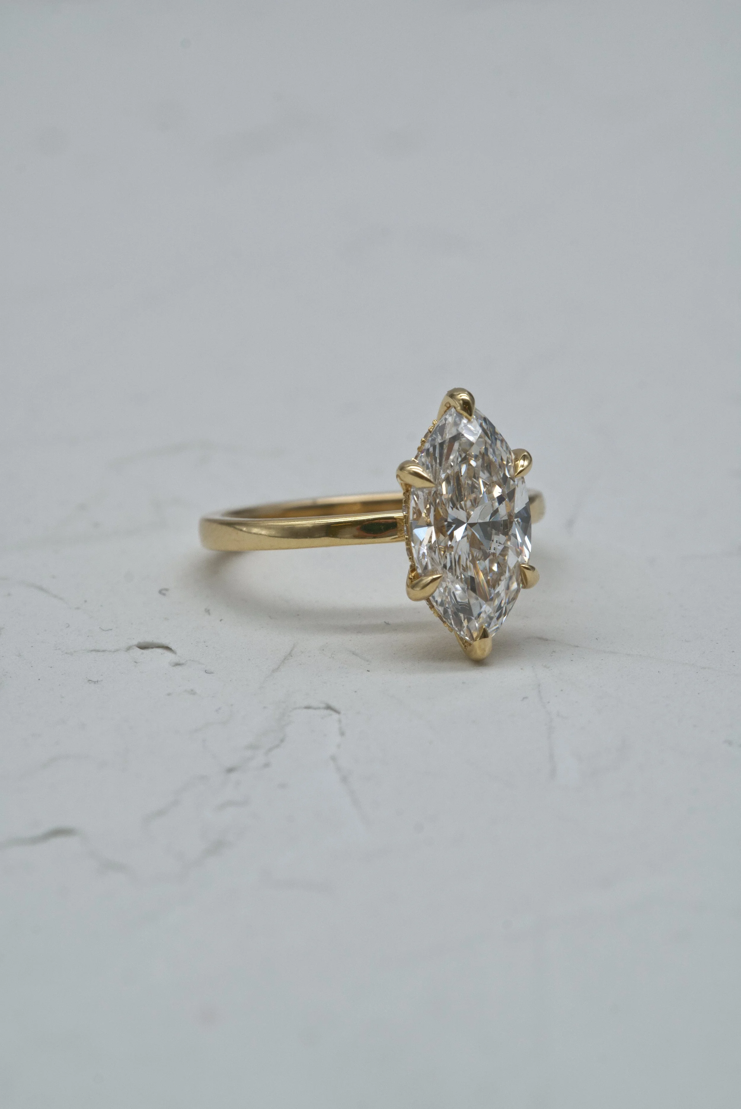 Close-up of a gold ring with a large marquise-cut diamond solitaire on a plain, light-colored surface