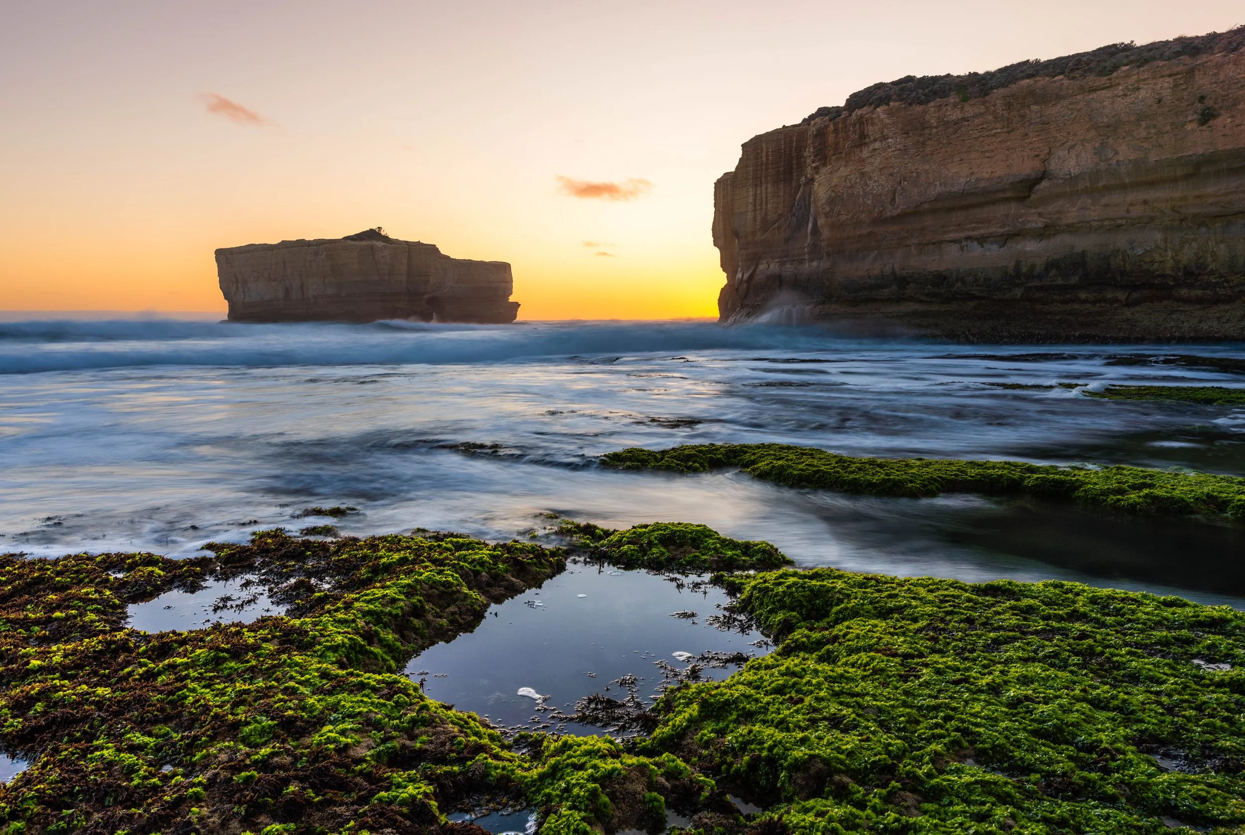 Sunset at Bakers Oven on the Great Ocean Road near Port Campbell, Victoria, with limestone cliffs, ocean waves and green seaweed-covered rocks.