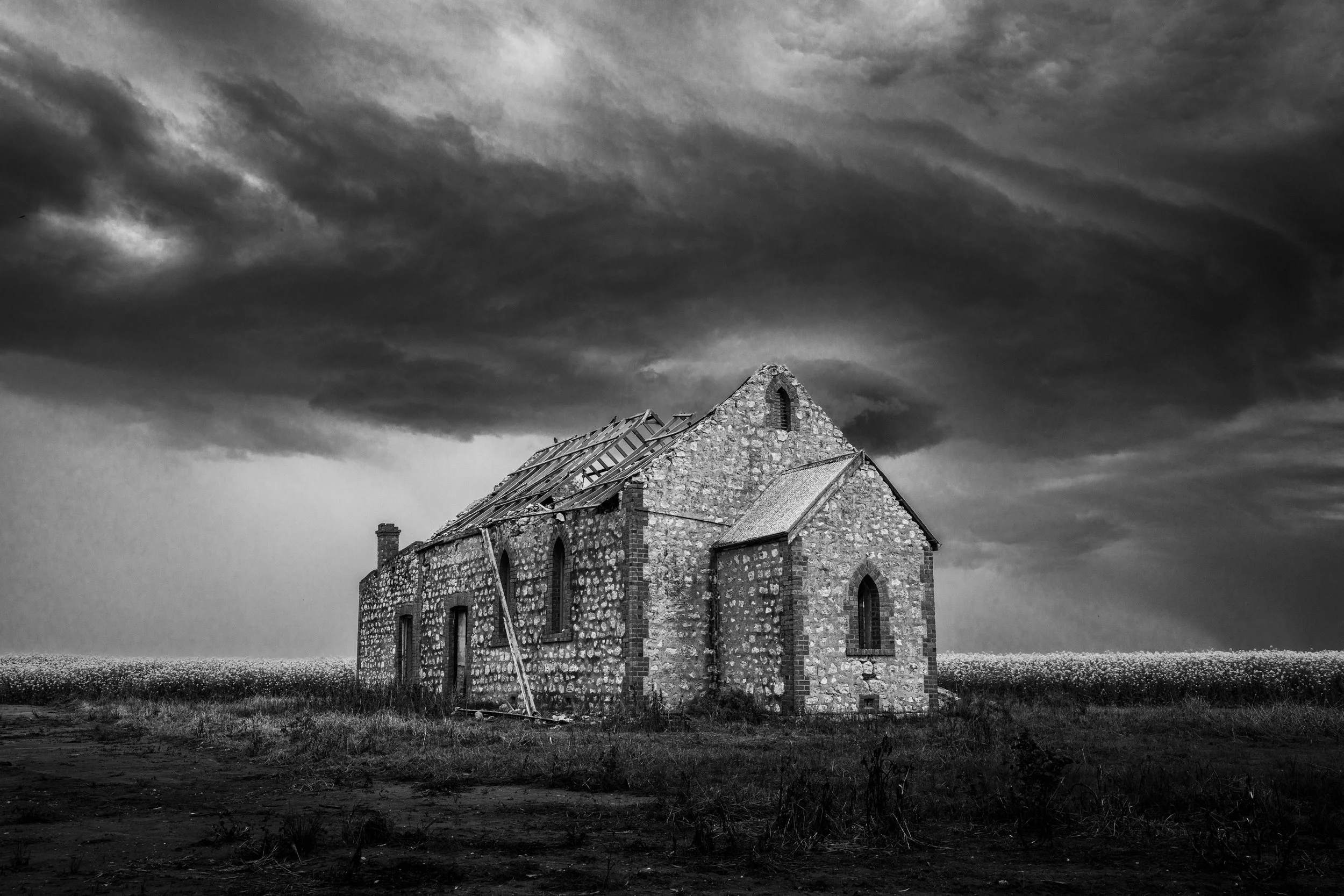 Black and white landscape photograph of an abandoned stone church beneath dramatic storm clouds near Hopetoun, Victoria.