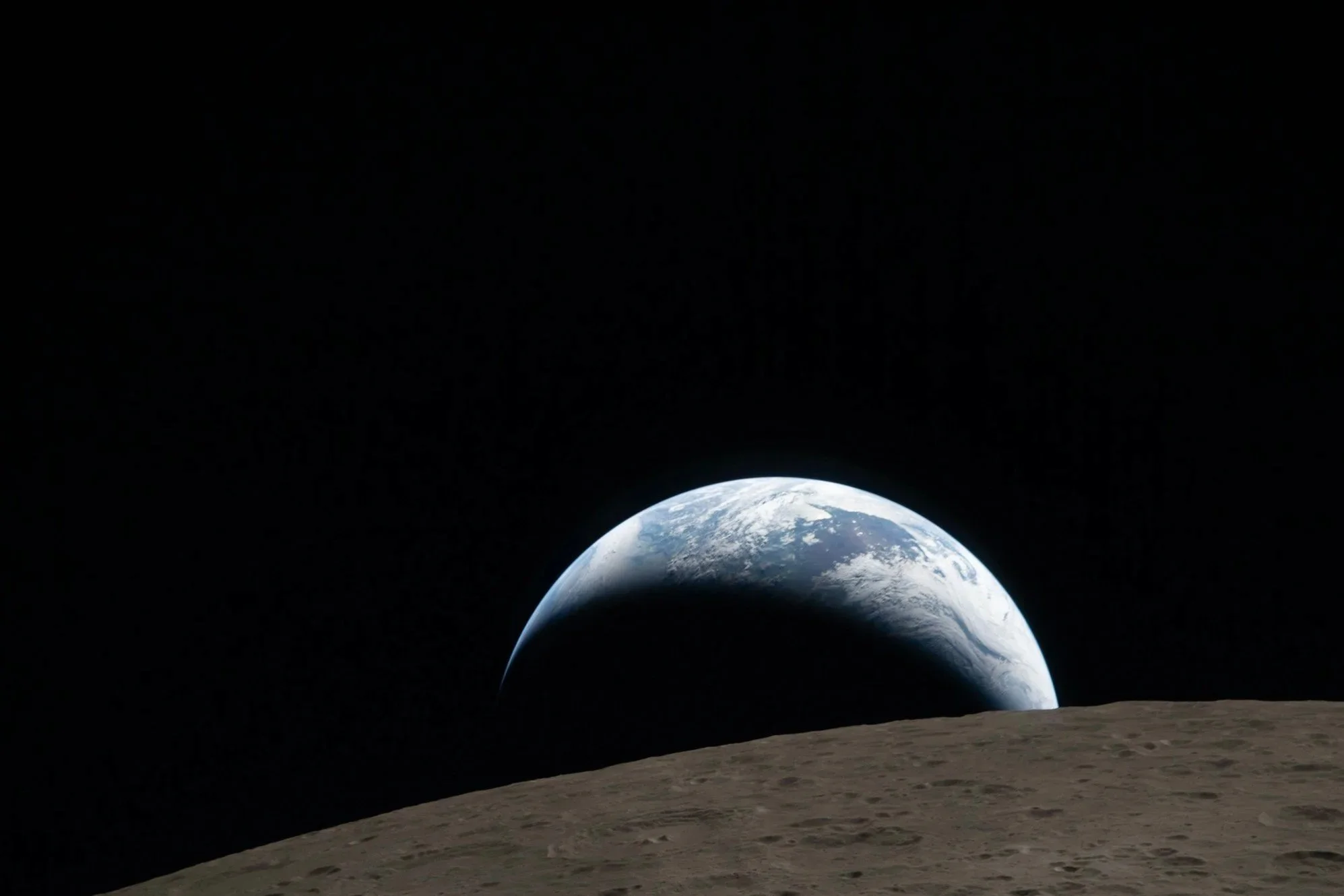 View of Earth from the Moon, with the lunar surface in the foreground and Earth in the distance against the blackness of space.