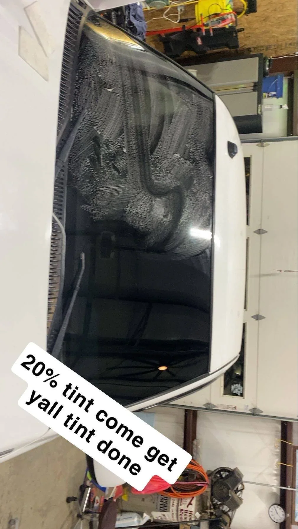 A vehicle with a tint film applied to the windows, partially cured, inside a garage. The garage contains tools, storage cabinets, and various items.