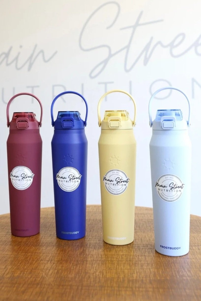 Four colorful insulated water bottles in pink, blue, yellow, and white, placed on a wooden surface with a blurred background featuring faint text.