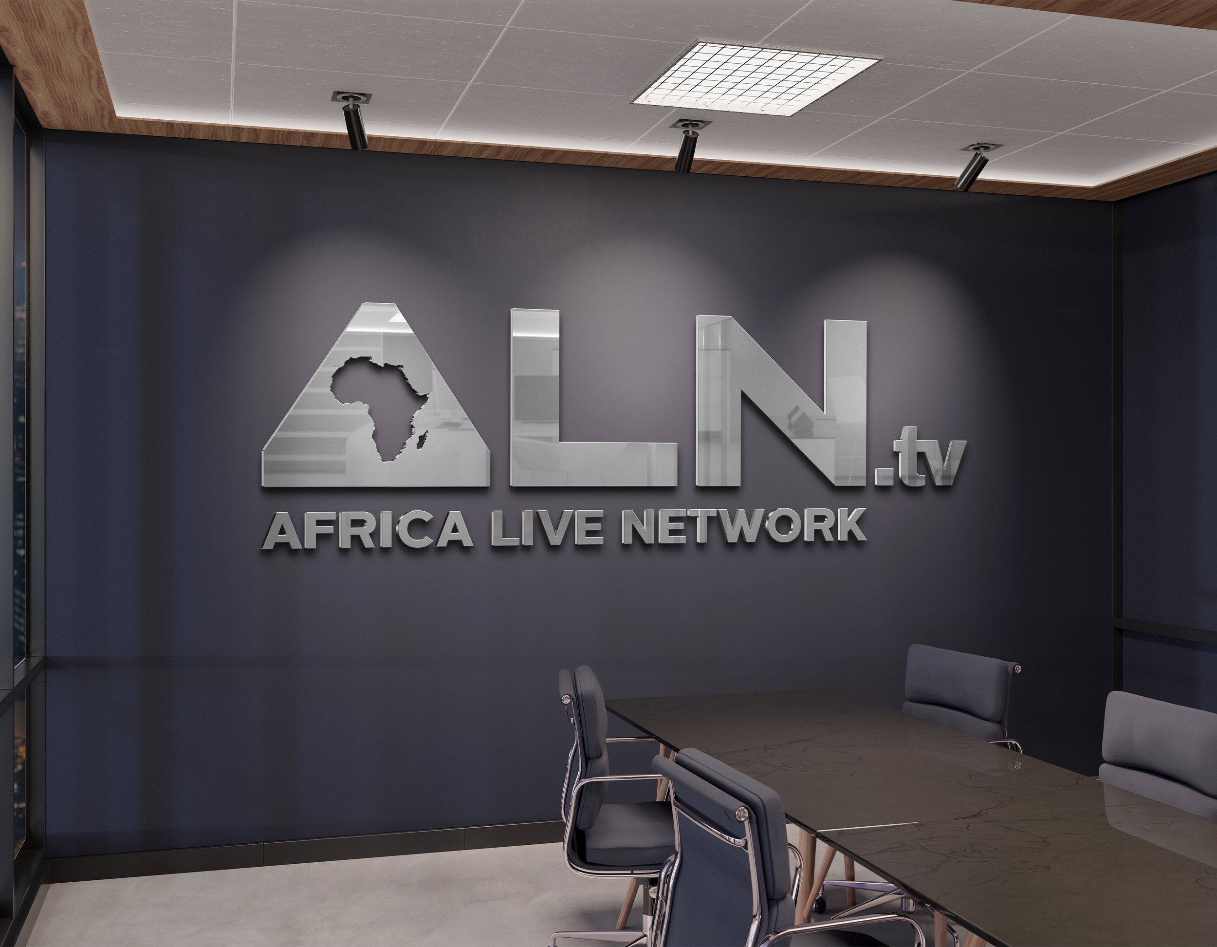 Interior of an office or conference room with a dark wall featuring a metal sign that says 'Africa Live Network' and a logo of the African continent. There are chairs arranged around a table and ceiling lights illuminate the room.