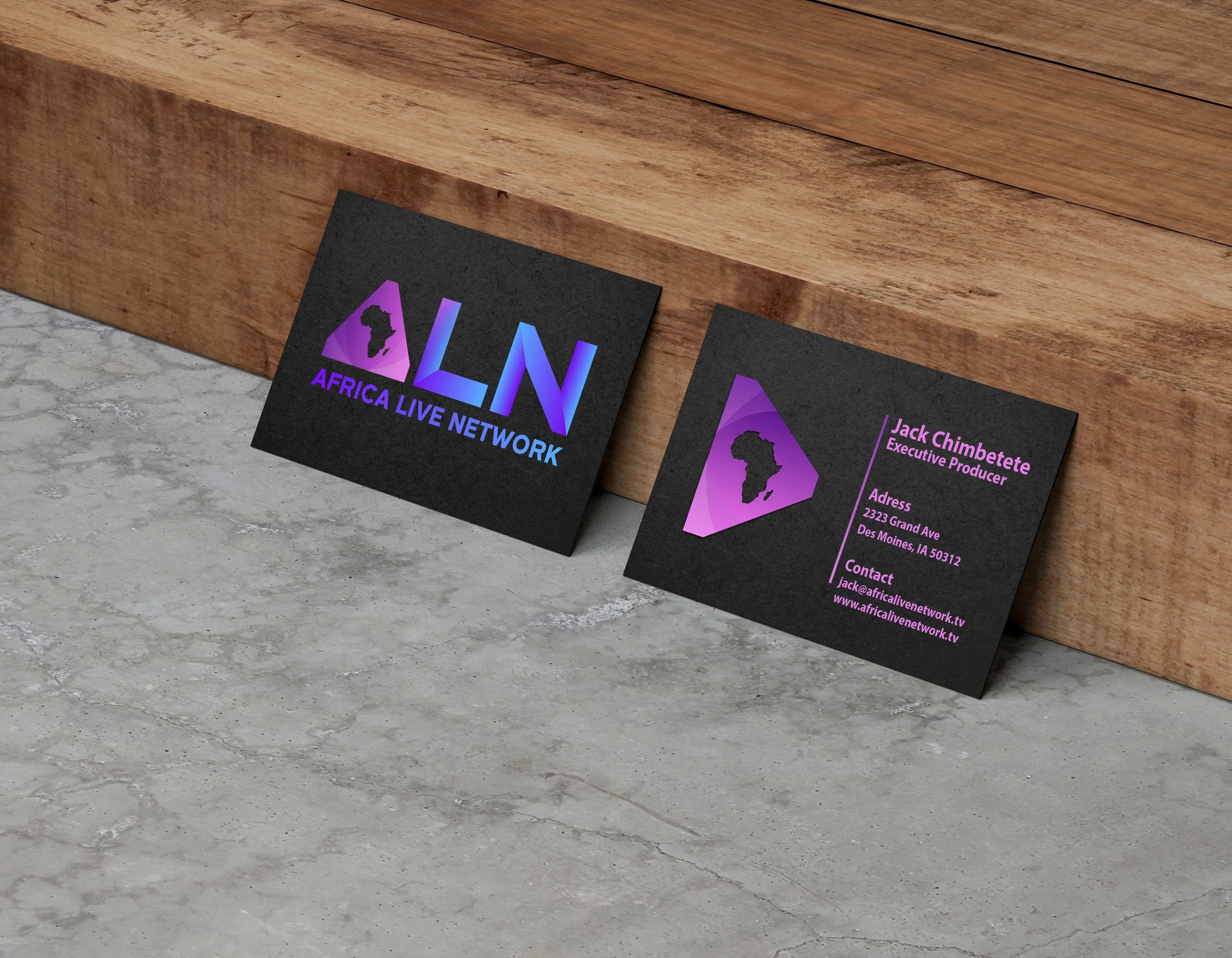 Business cards for Africa Live Network placed on a wooden surface. The cards display a logo with the shape of Africa and the text 'ALN' in gradient purple and blue colors, along with contact information including an email address and website.