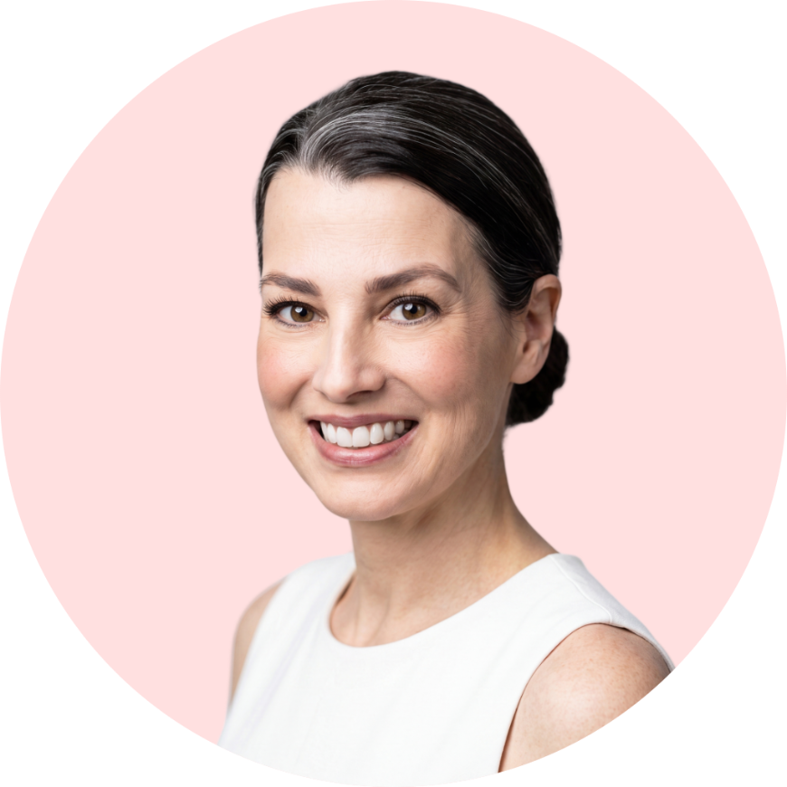Close-up of a woman smiling with dark hair tied back, wearing a white sleeveless top, against a pink background.