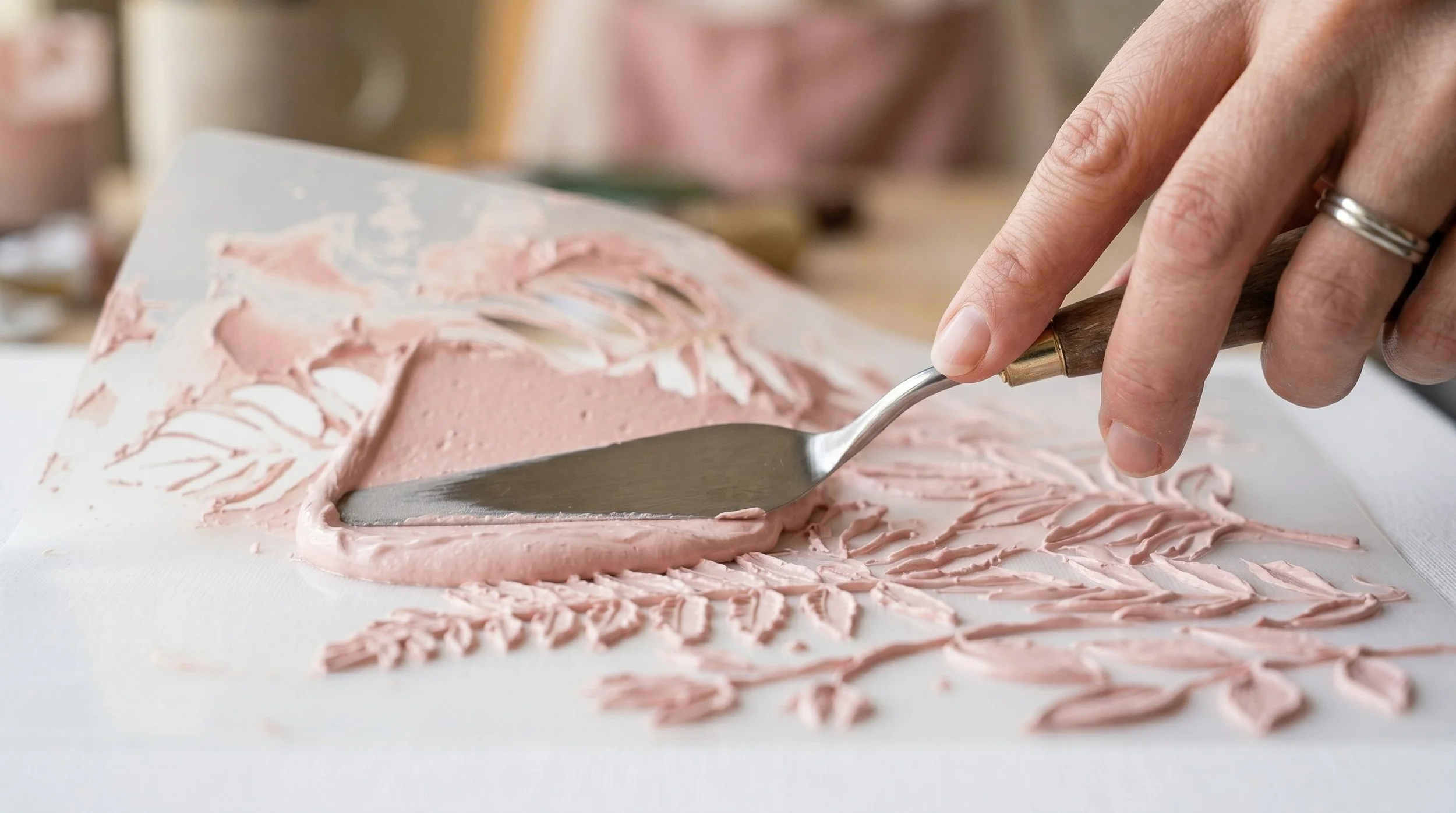A person spreading pink frosting on a cake with a palette knife, creating decorative patterns.