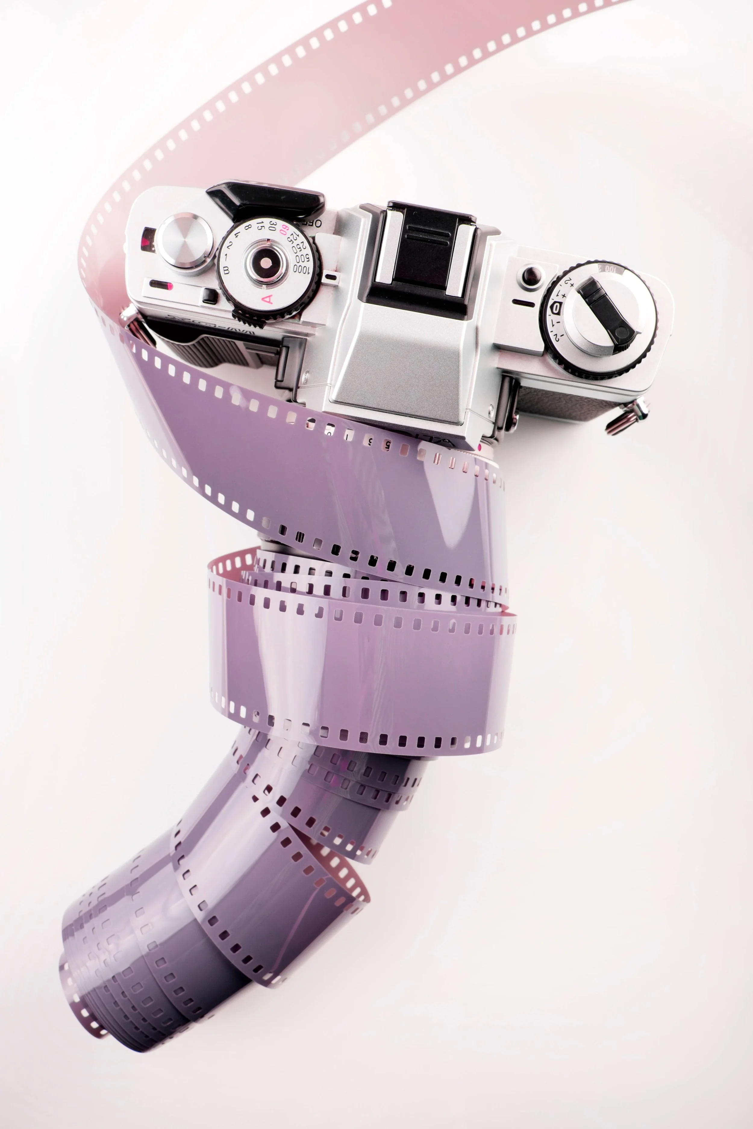 A vintage camera placed on a strand of pink and purple photographic film, with the film unwinding in a spiral shape.