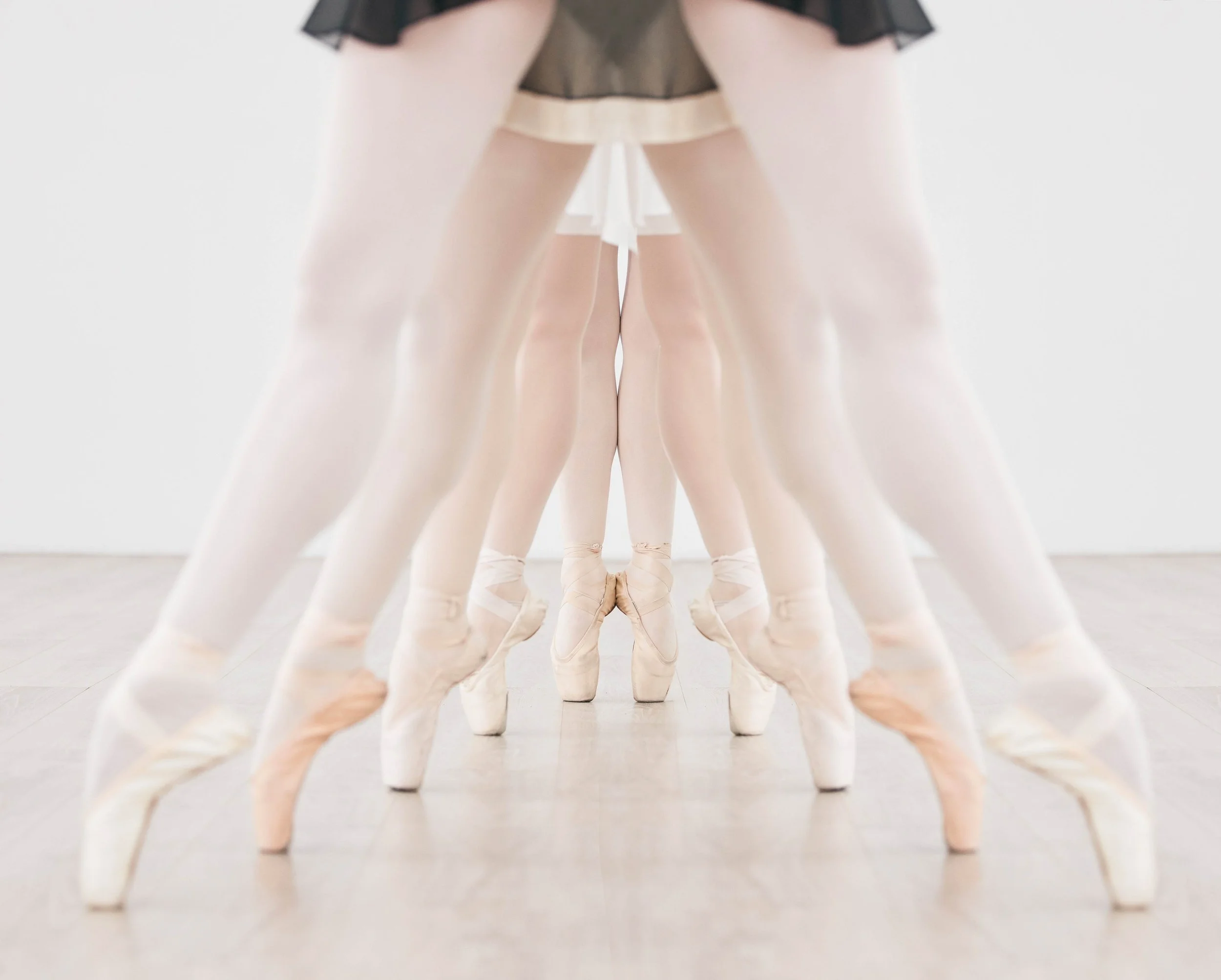 A mirrored image of ballet dancers in pointe shoes and tutus, standing in a ballet studio.