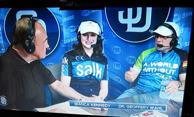 Three people wearing headsets engaged in a broadcast interview at a sports event, with a backdrop displaying the San Diego Padres and Los Angeles Dodgers logos.