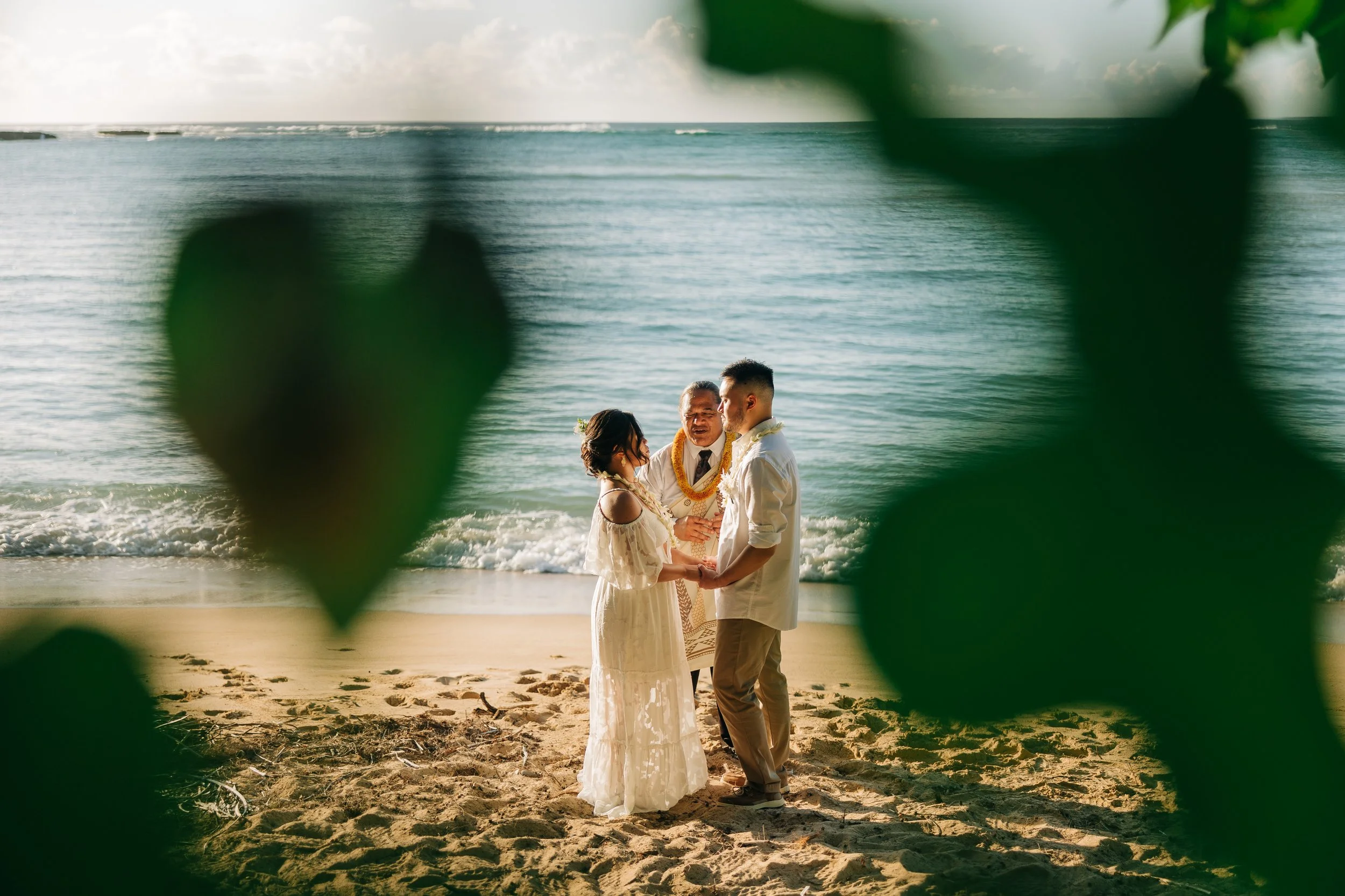 A couple enjoy a quiet moment with their officiant under the soft late afternoon light on the North Shore of Oahu
