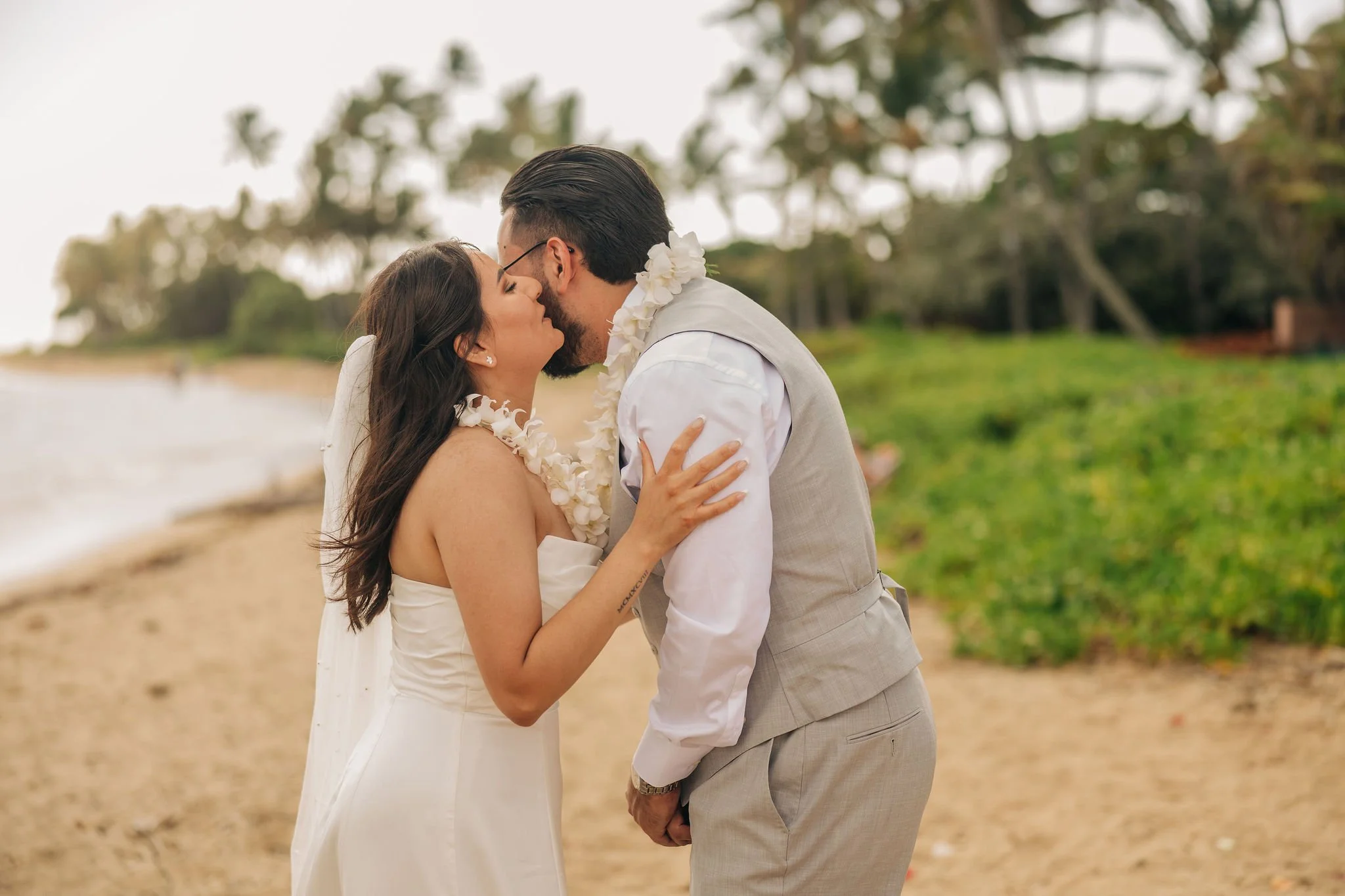 A couple on the beach dressed in wedding attire, about to kiss.